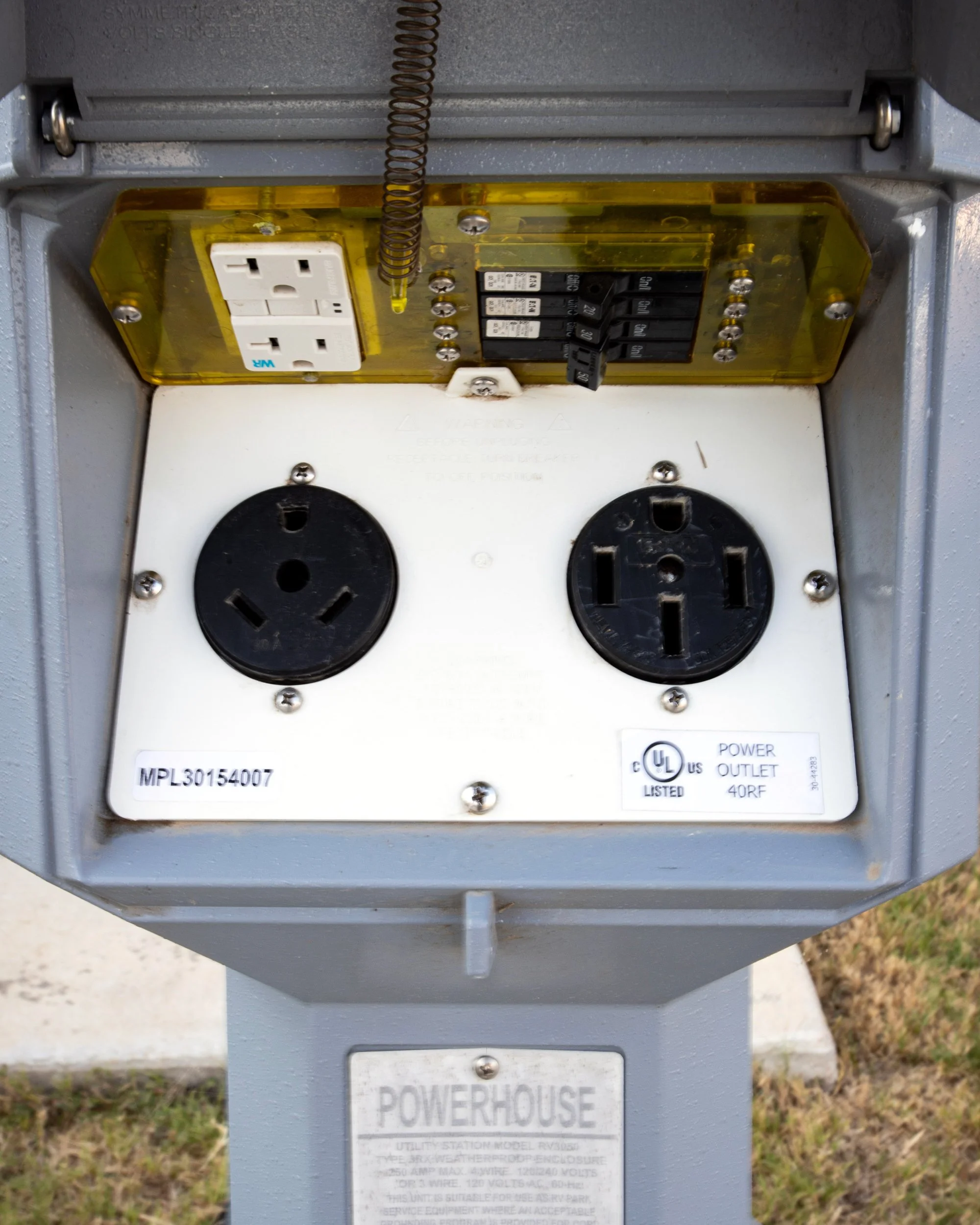 Close-up of an outdoor electrical power outlet box with multiple power outlets and circuit breakers, mounted on a gray metal pole.