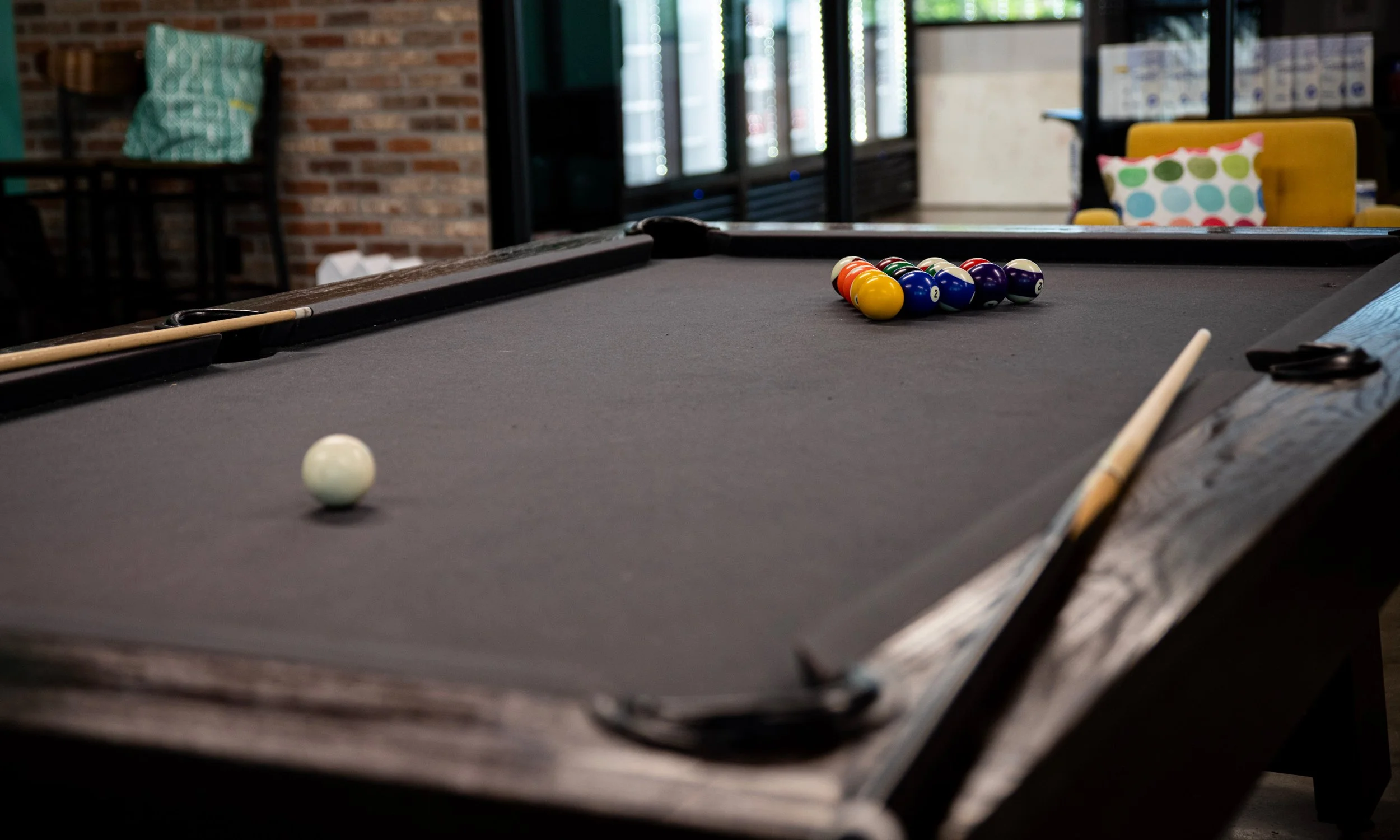 A pool table with a triangle rack of striped and solid billiard balls arranged for a game, and a cue stick resting on the side.
