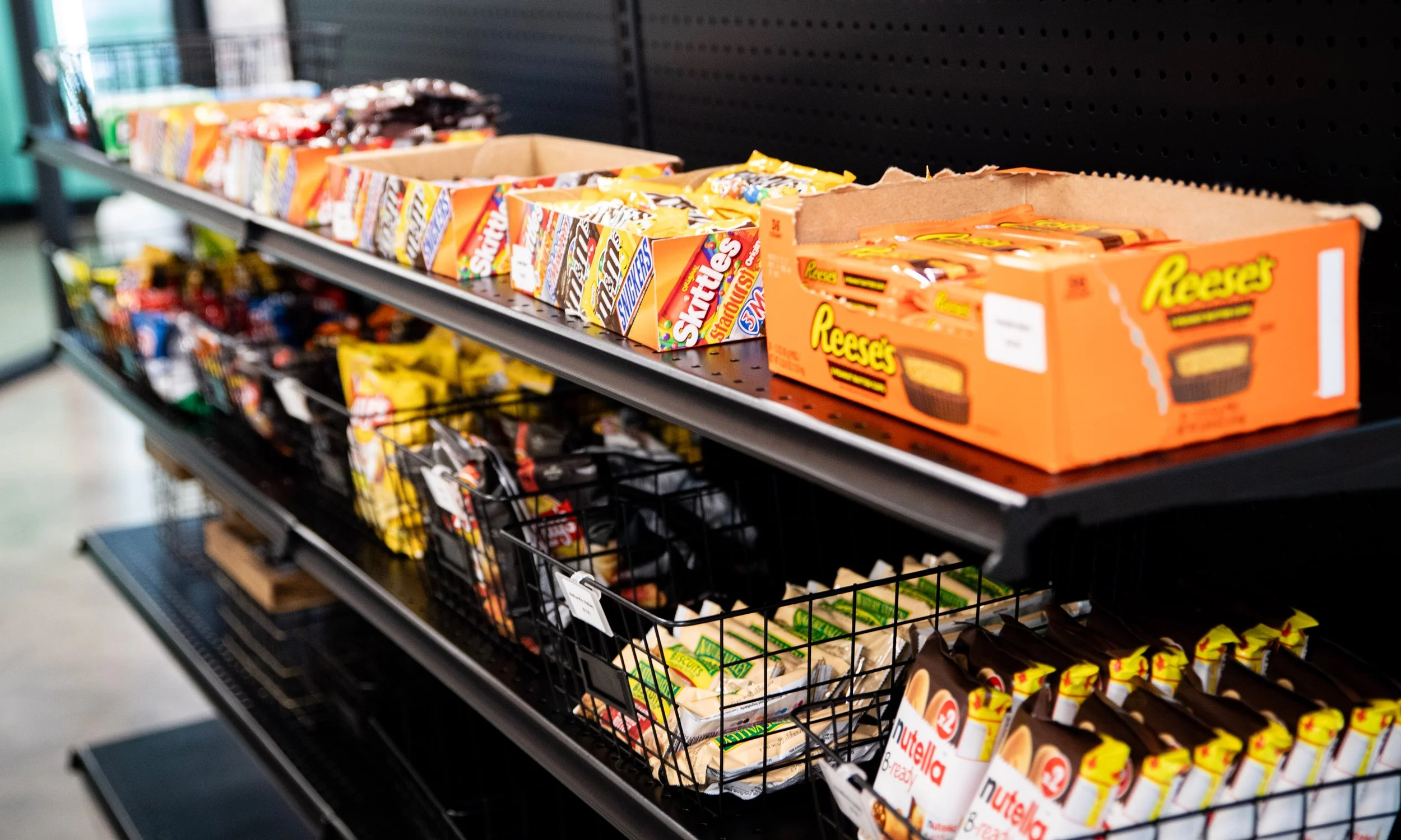 Assorted candy bars on black metal shelves in a store.