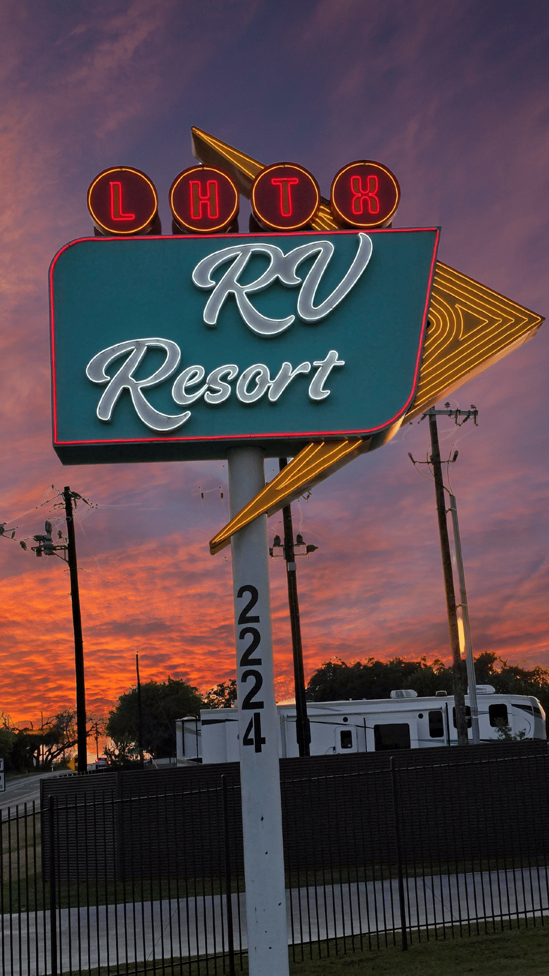 Neon-lit sign for RV resort with a sunset sky in the background.