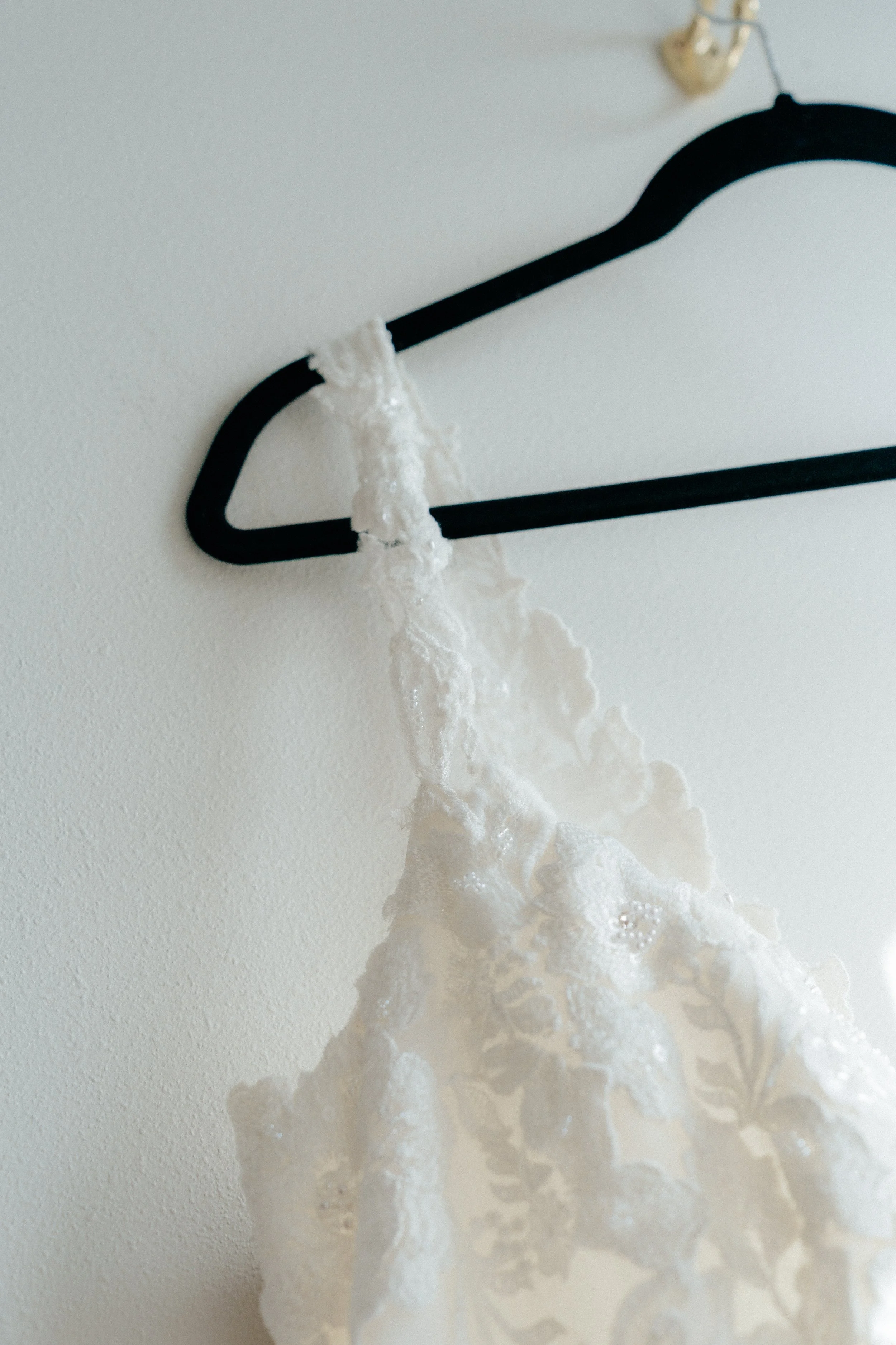 Close-up of a coat hanger with dried lace fabric hanging from it, mounted on a white wall.