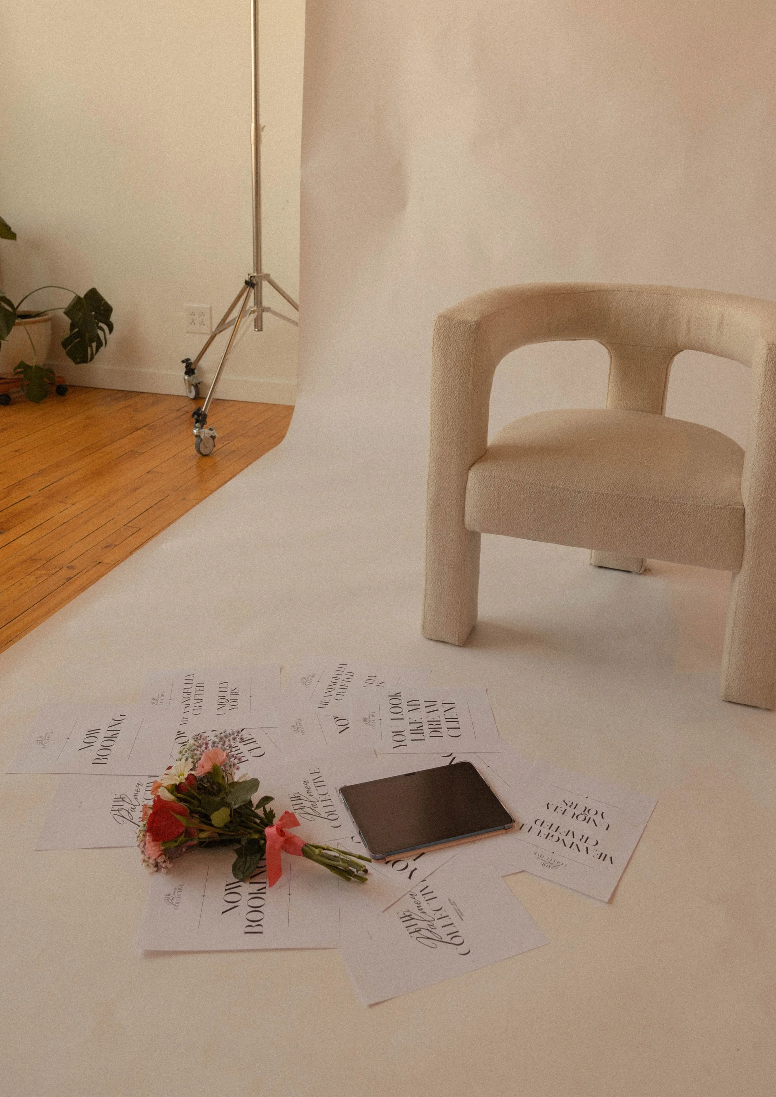 A bouquet of pink and orange roses with green leaves on a white surface scattered with printed pages that have 'You look like a dream come true' written on them. In the background, there is a beige chair, a potted plant, and a light-colored wall.