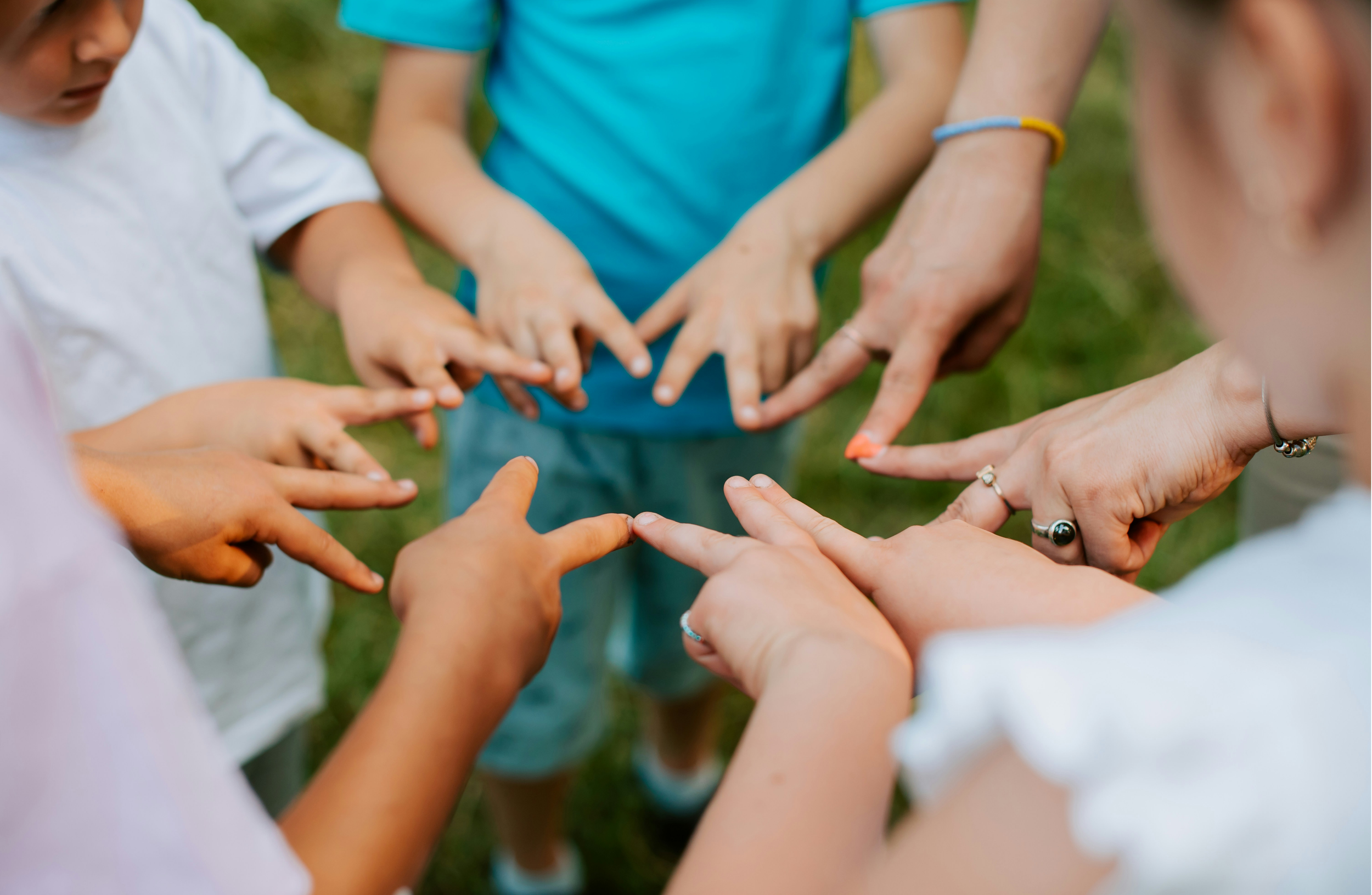 Multiple people putting their hands together in a circle outdoors, symbolizing teamwork or unity.