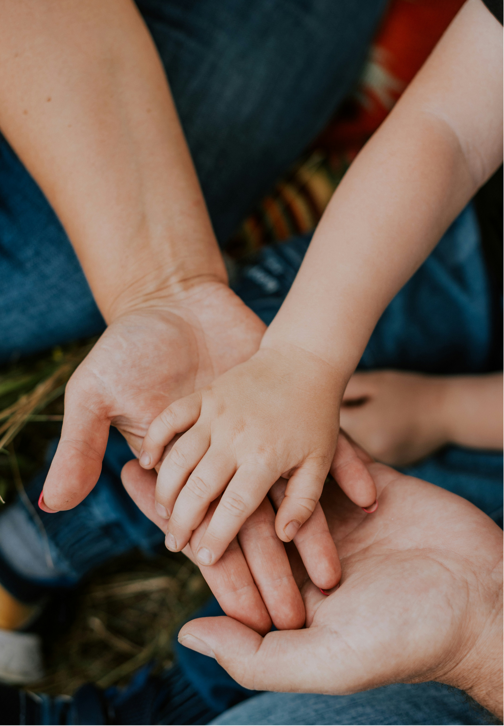 Multiple hands of different ages stacked together, symbolizing unity and teamwork, with a blurred outdoor background.