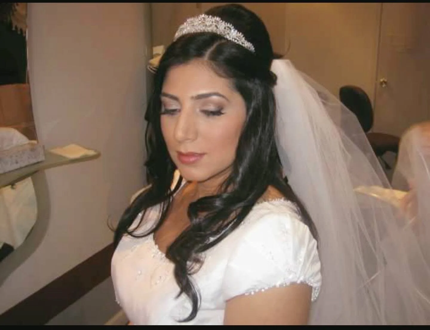 Portrait of a bride with black hair wearing a wedding dress, veil, and tiara, with eyes closed and a peaceful expression.