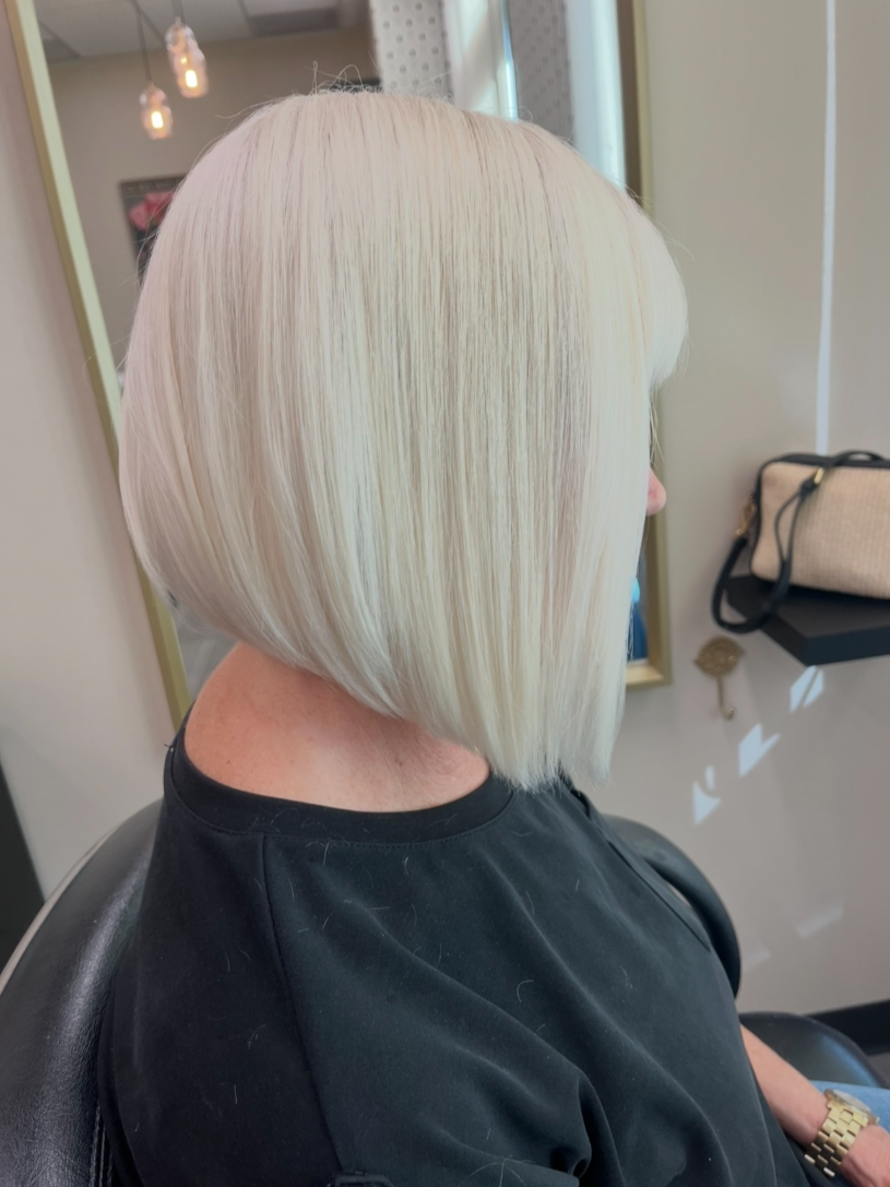 A woman with straight, platinum blonde bob haircut sitting in a salon chair.