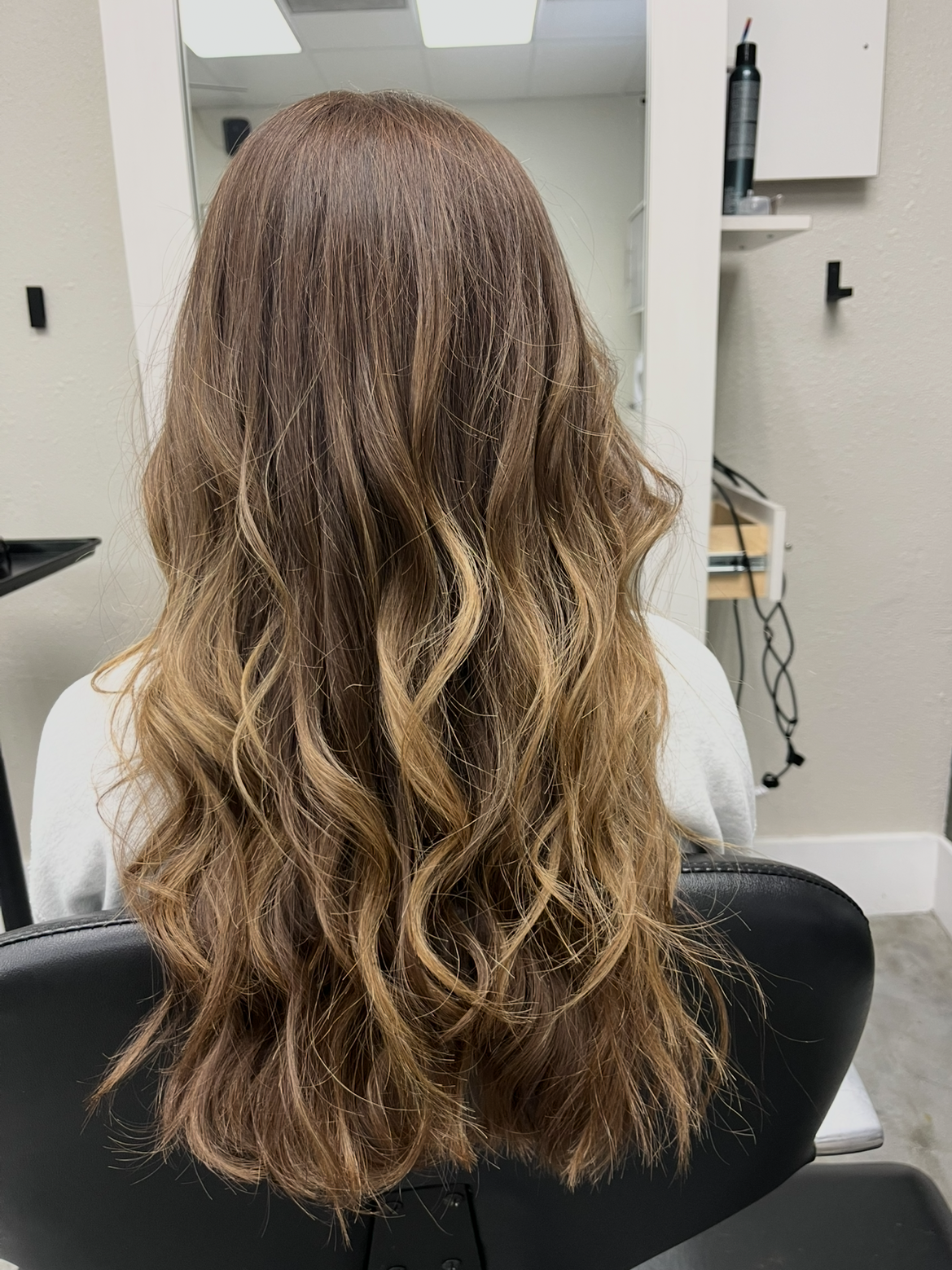 Back of a person with long, wavy, light brown hair sitting in a salon chair.