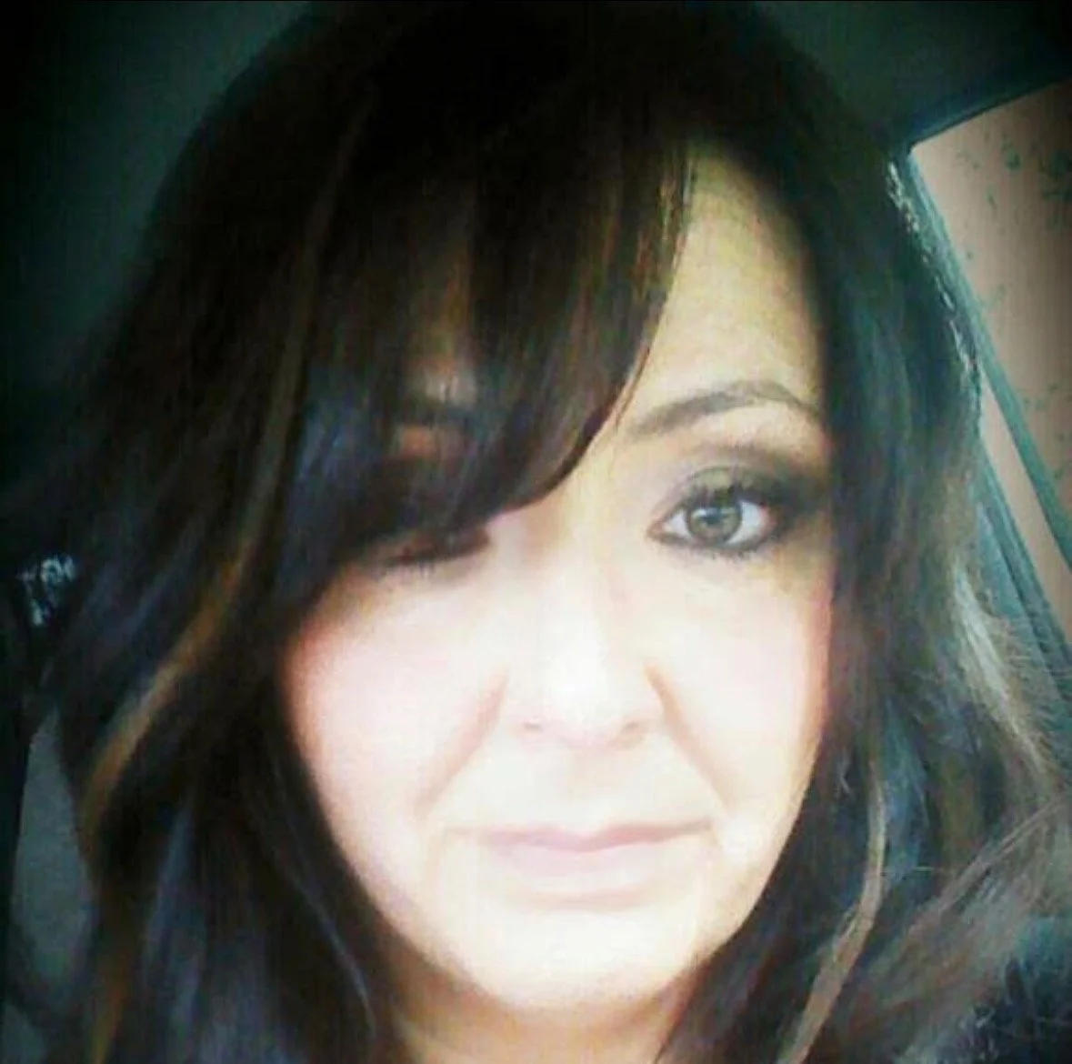 Close-up of a woman with long dark hair, one eye visible, in a vehicle.