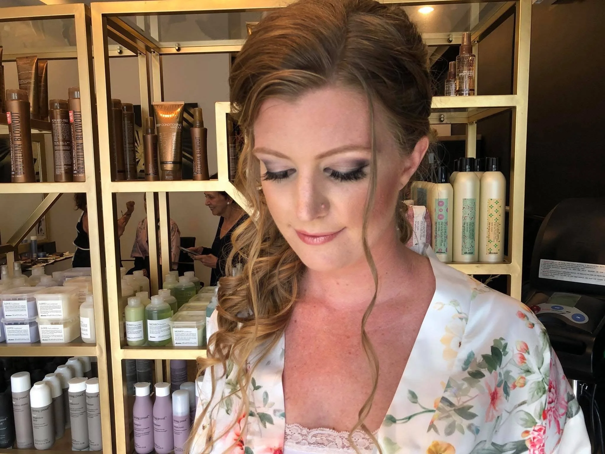Woman with long, wavy hair and floral dress standing in front of shelves of hair care products.
