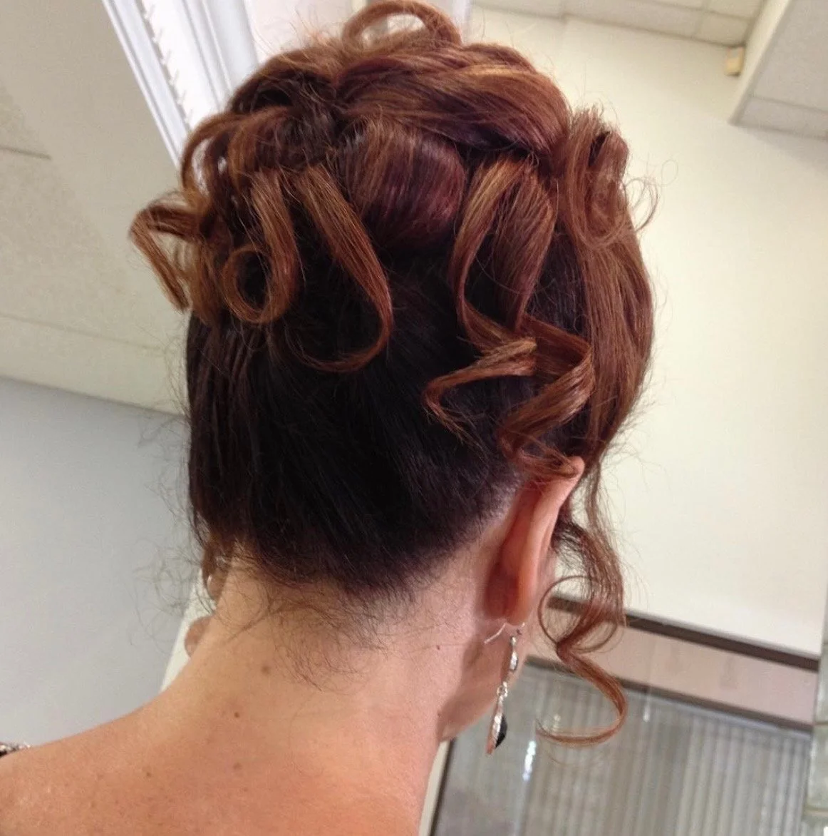 Back of a person's head with short black hair at the nape and styled, curly, reddish-brown hair on top.