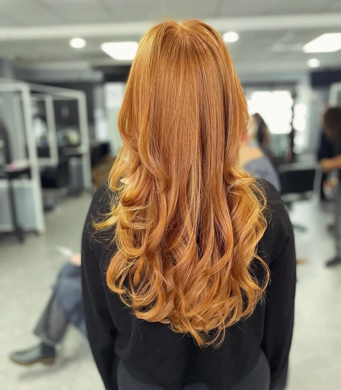 Back view of a woman with long, wavy, red hair in a salon or similar setting.