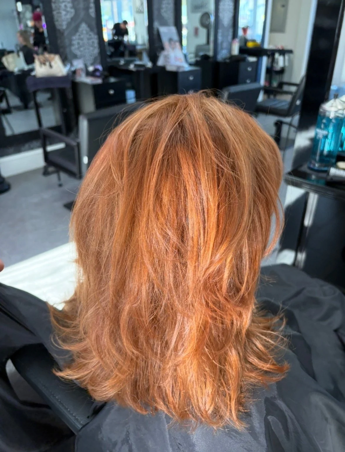 Back view of a person with shoulder-length, wavy, red-orange hair in a hair salon.