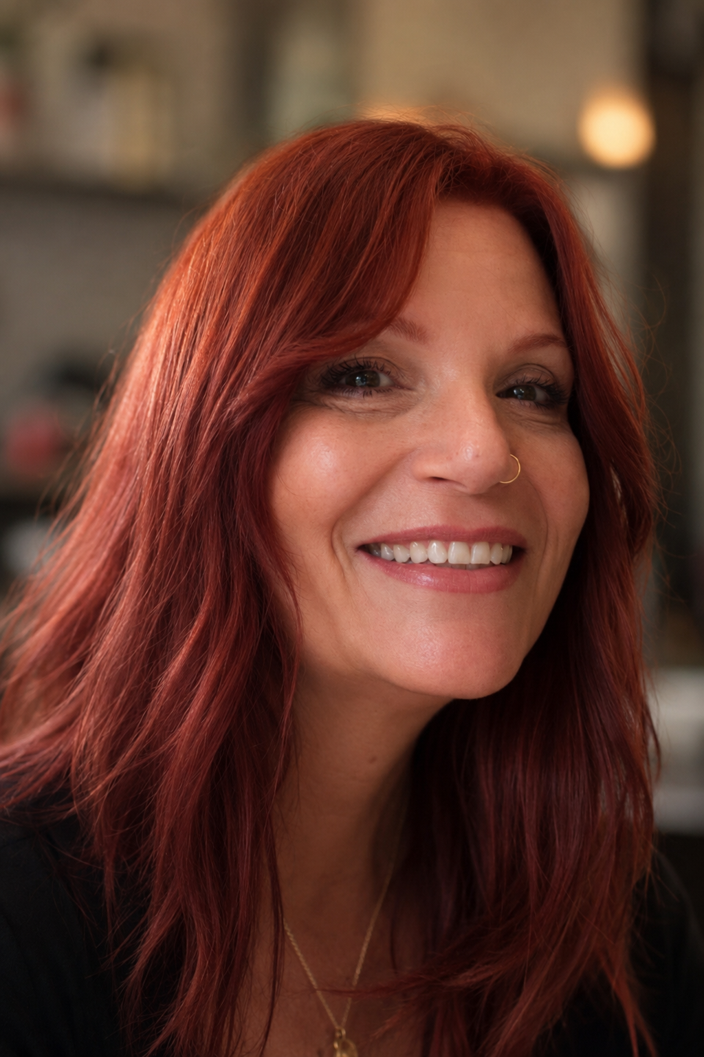 A woman with long red hair smiling in an indoor setting.