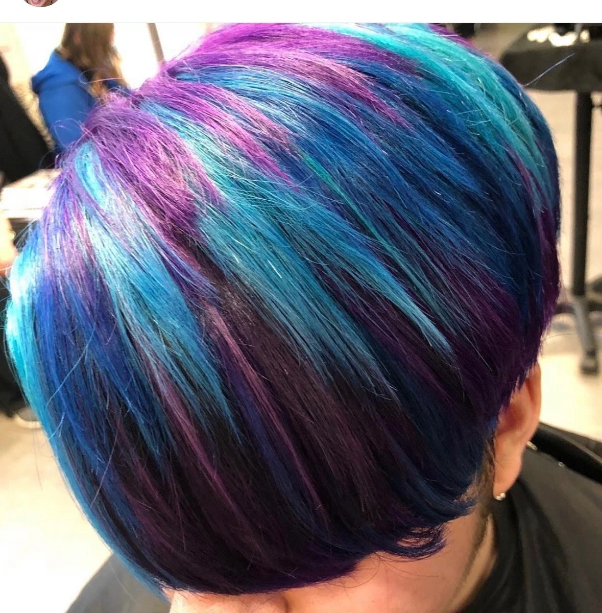 Close-up of a person's hair dyed with vibrant shades of purple, blue, and teal, styled in a sleek, shiny bob.