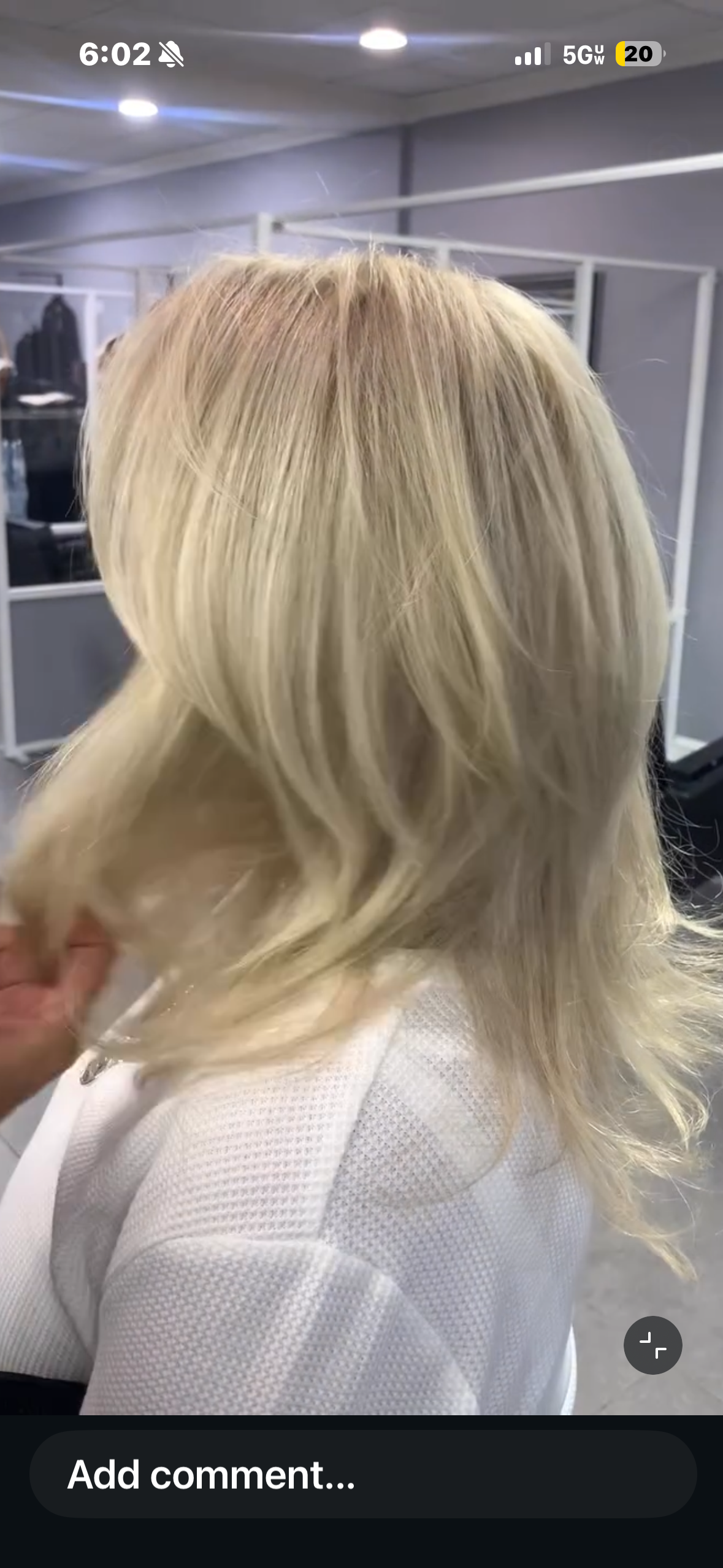 Blonde hair styled in loose waves on a woman in a white textured top, in a salon or similar setting.