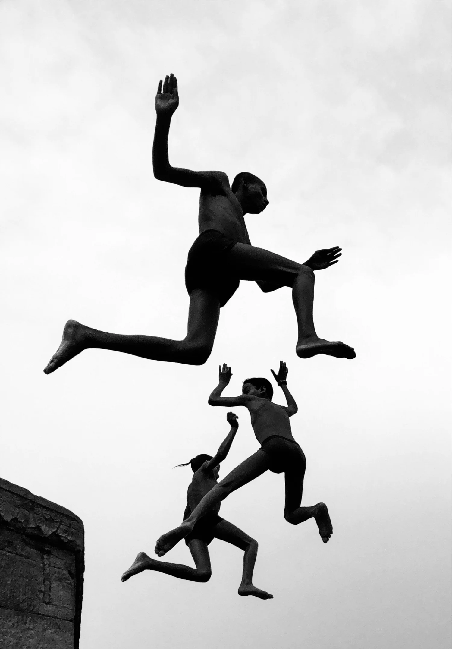 Three boys silhouetted in mid-leap against a blank white sky, bodies fully extended, faces not legible
