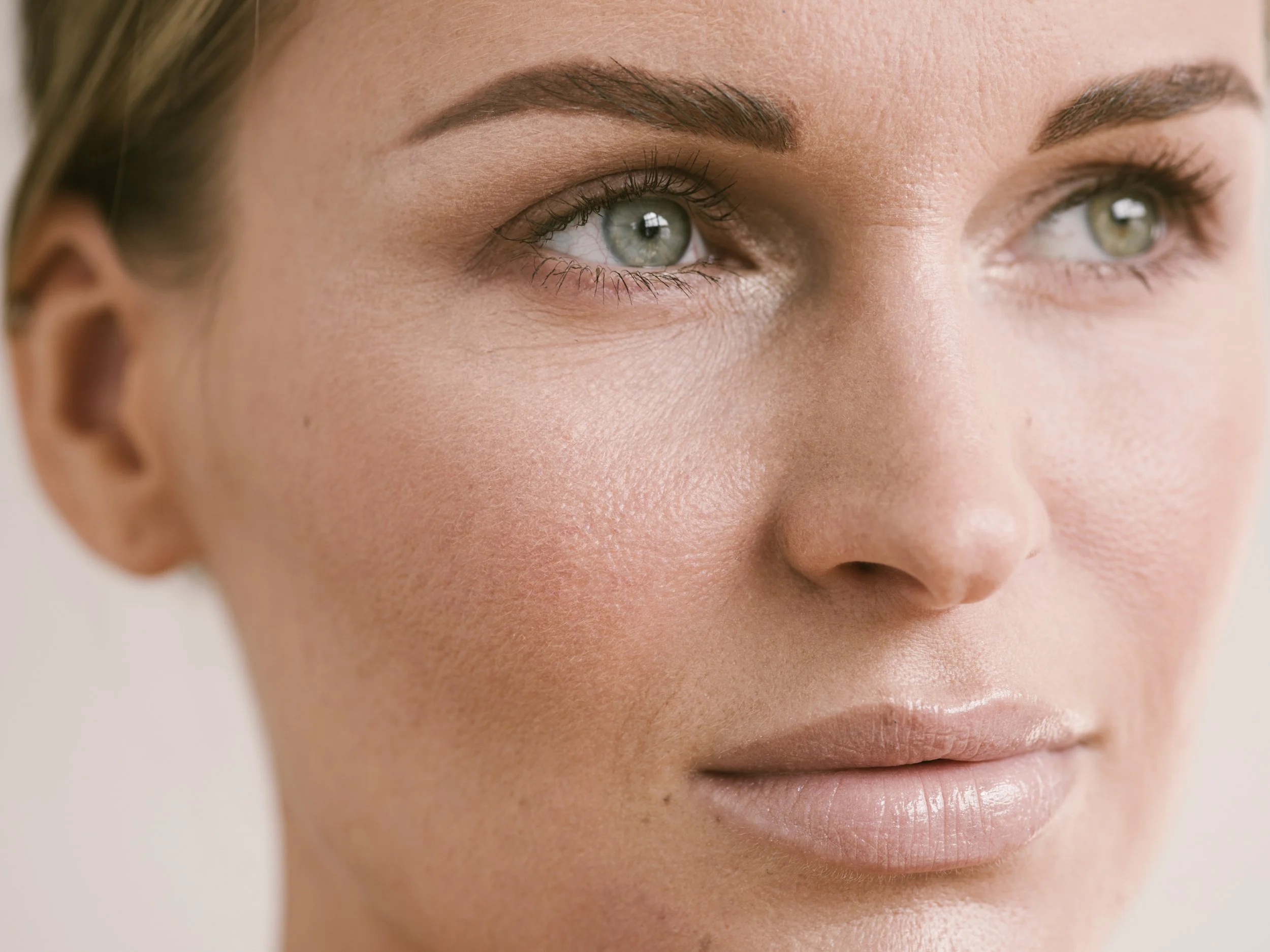 Close-up of a woman's face focusing on her blue-green eye, eyebrow, and lips.
