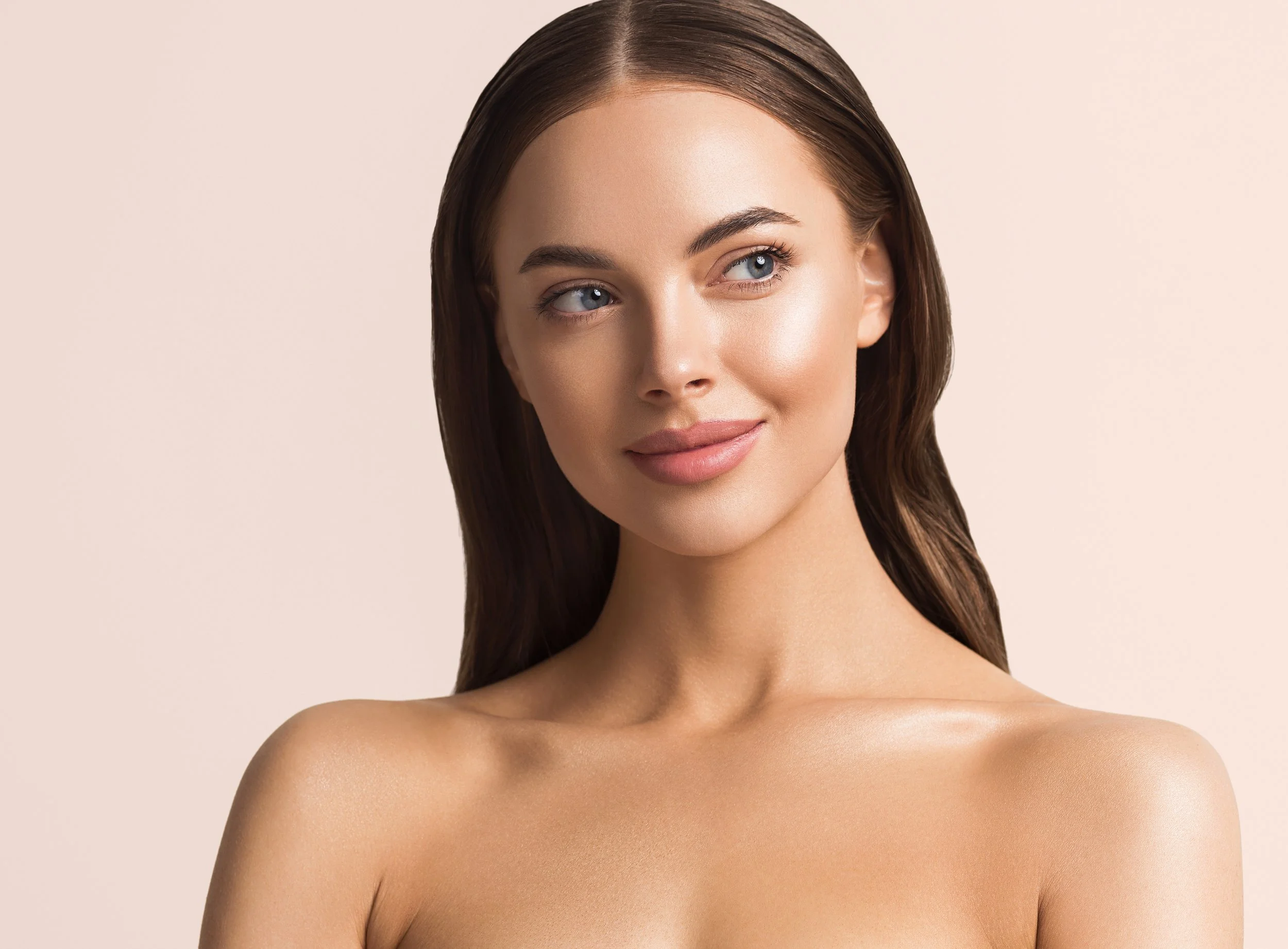 Portrait of a young woman with long brown hair, blue eyes, and smooth skin, looking slightly to the side against a plain beige background.