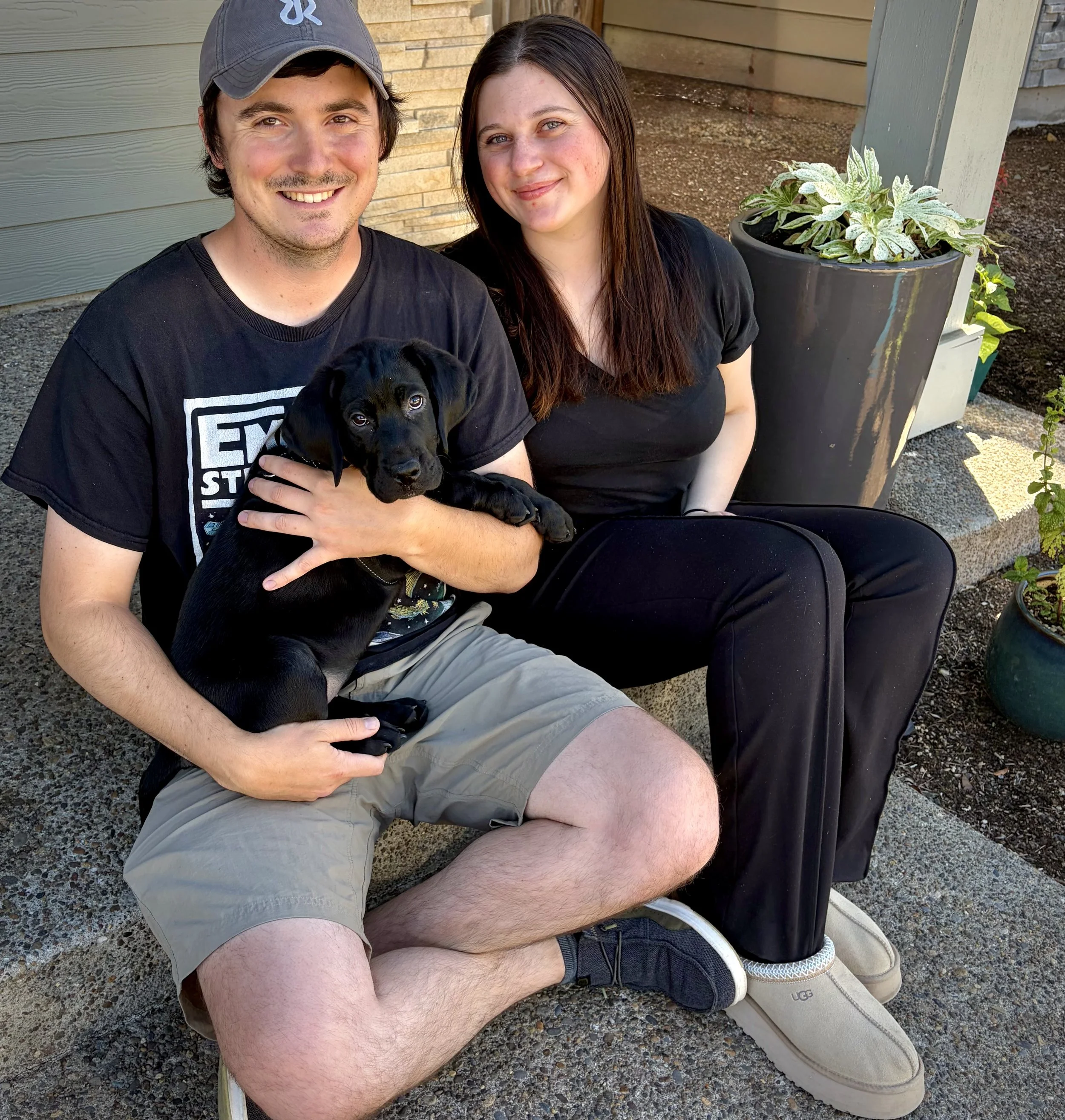 Founders Matt and Lorna sitting outdoors with Sitka, their black Labrador puppy and the inspiration behind Sitka Roasting Co.