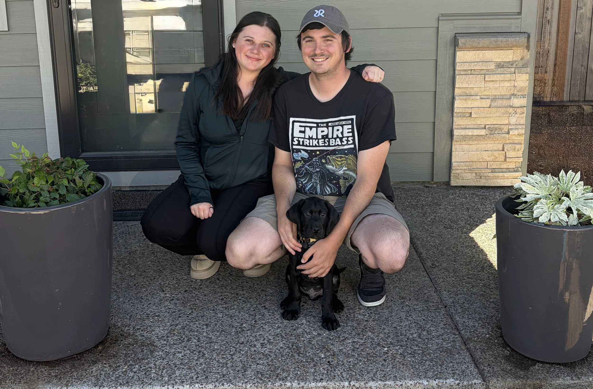Founders Matt and Lorna sitting outdoors with Sitka, their black Labrador puppy, and the inspiration behind Sitka Roasting Co.
