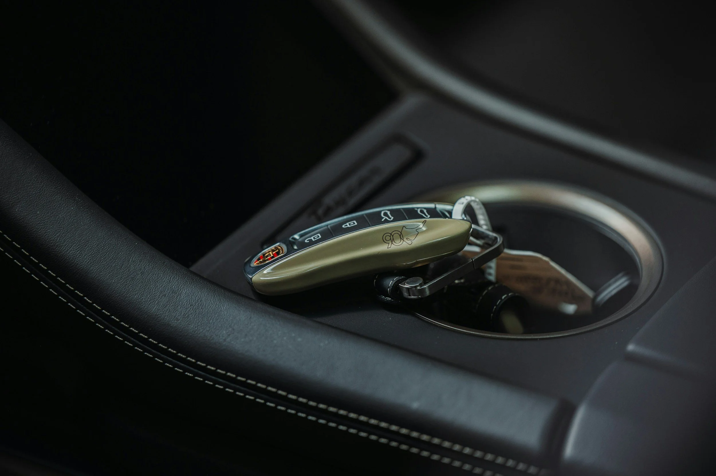 A car key fob with a silver and beige design resting on a car's center console near a circular gear shift knob.