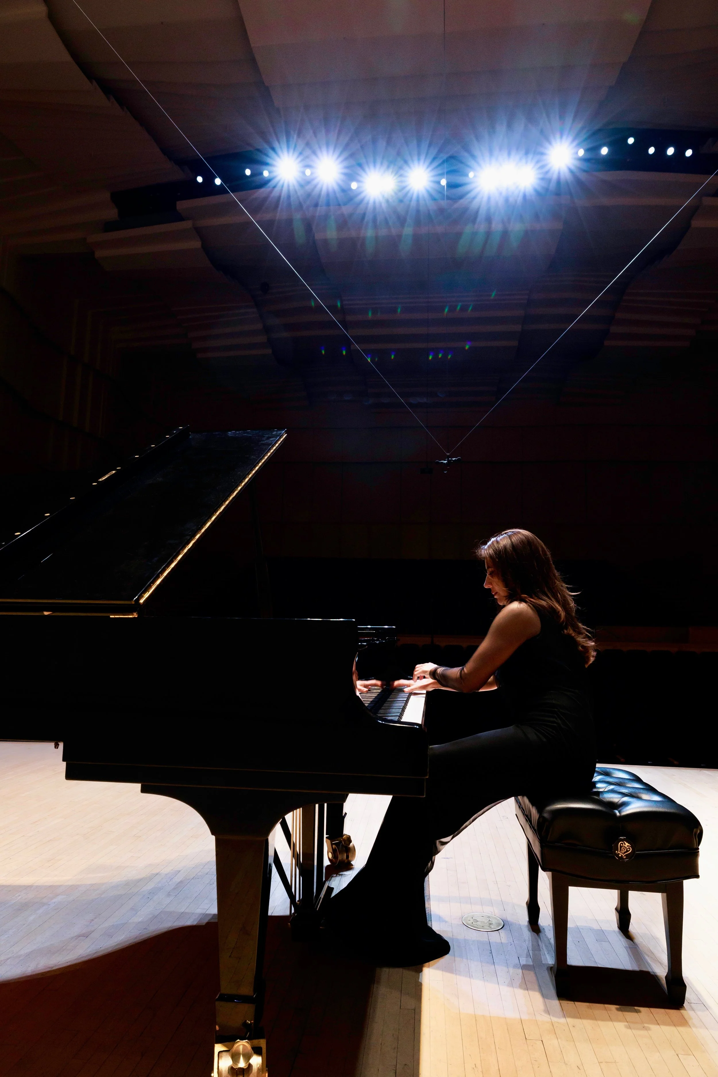 A woman playing the piano on stage, with stage lights above and a wooden ceiling.