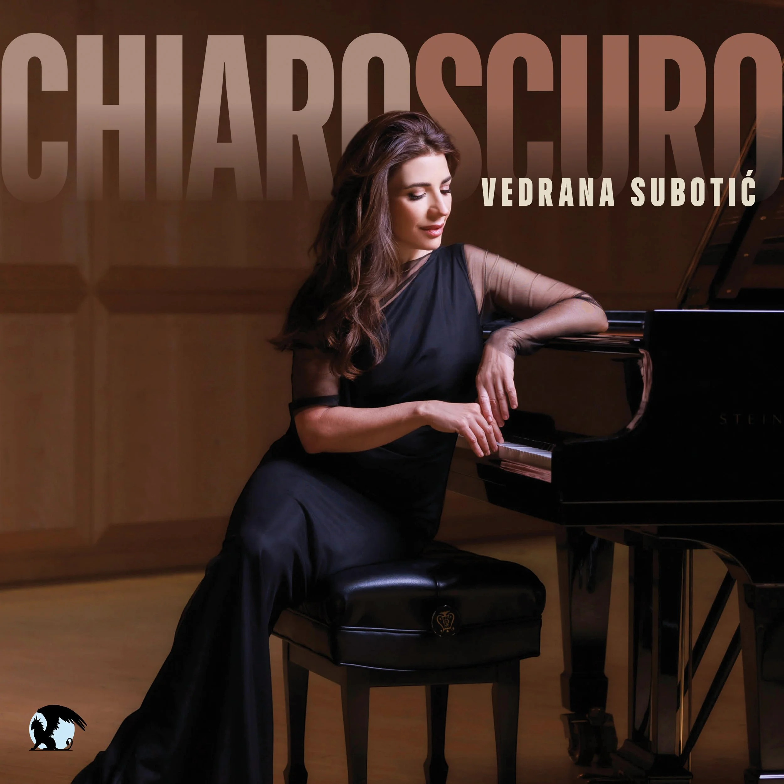 A woman with long wavy brown hair is playing a grand piano in a dimly lit room. She is wearing a black dress with sheer sleeves and is focused on the piano keys.