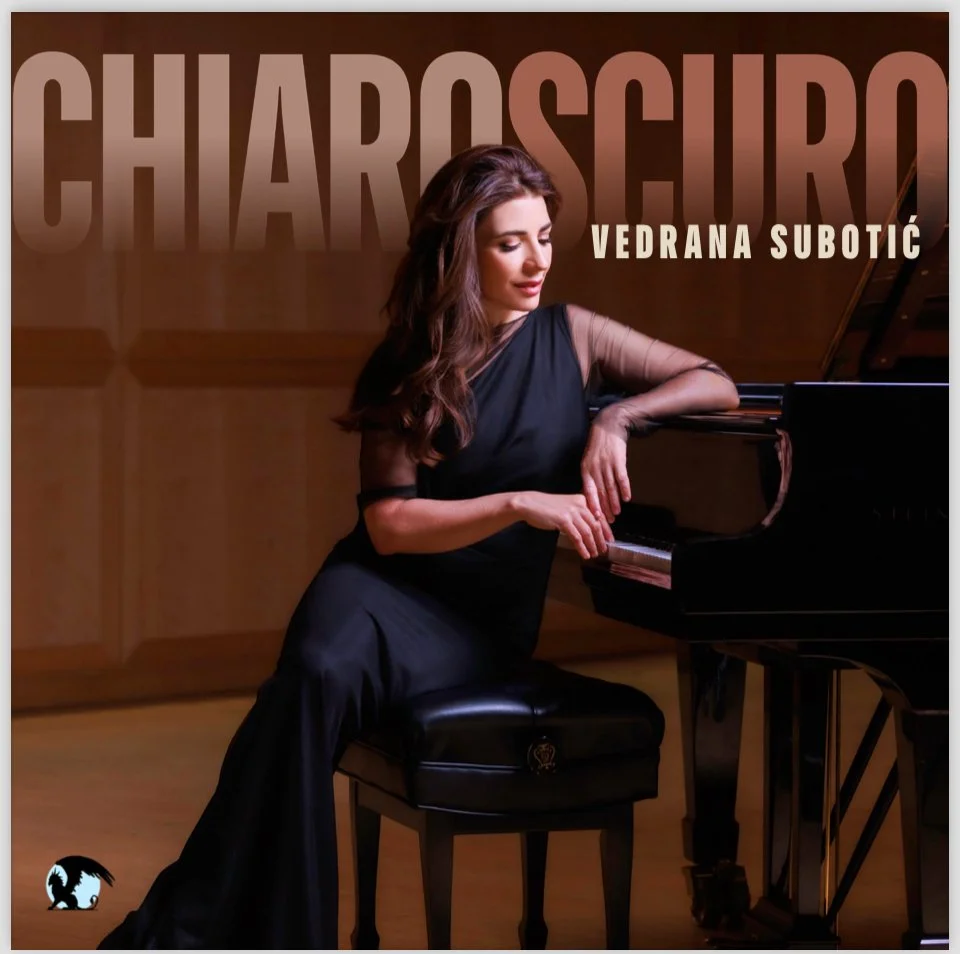A woman in a black dress sitting at a grand piano, looking down with a serene expression.