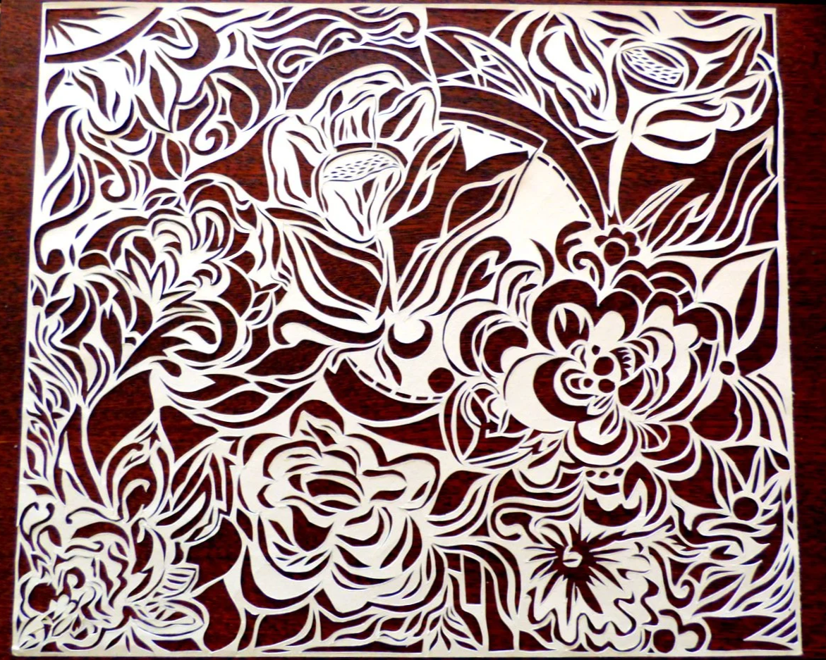 A detailed paper cut-out featuring intricate floral and botanical patterns, with various flowers, leaves, and swirling designs.