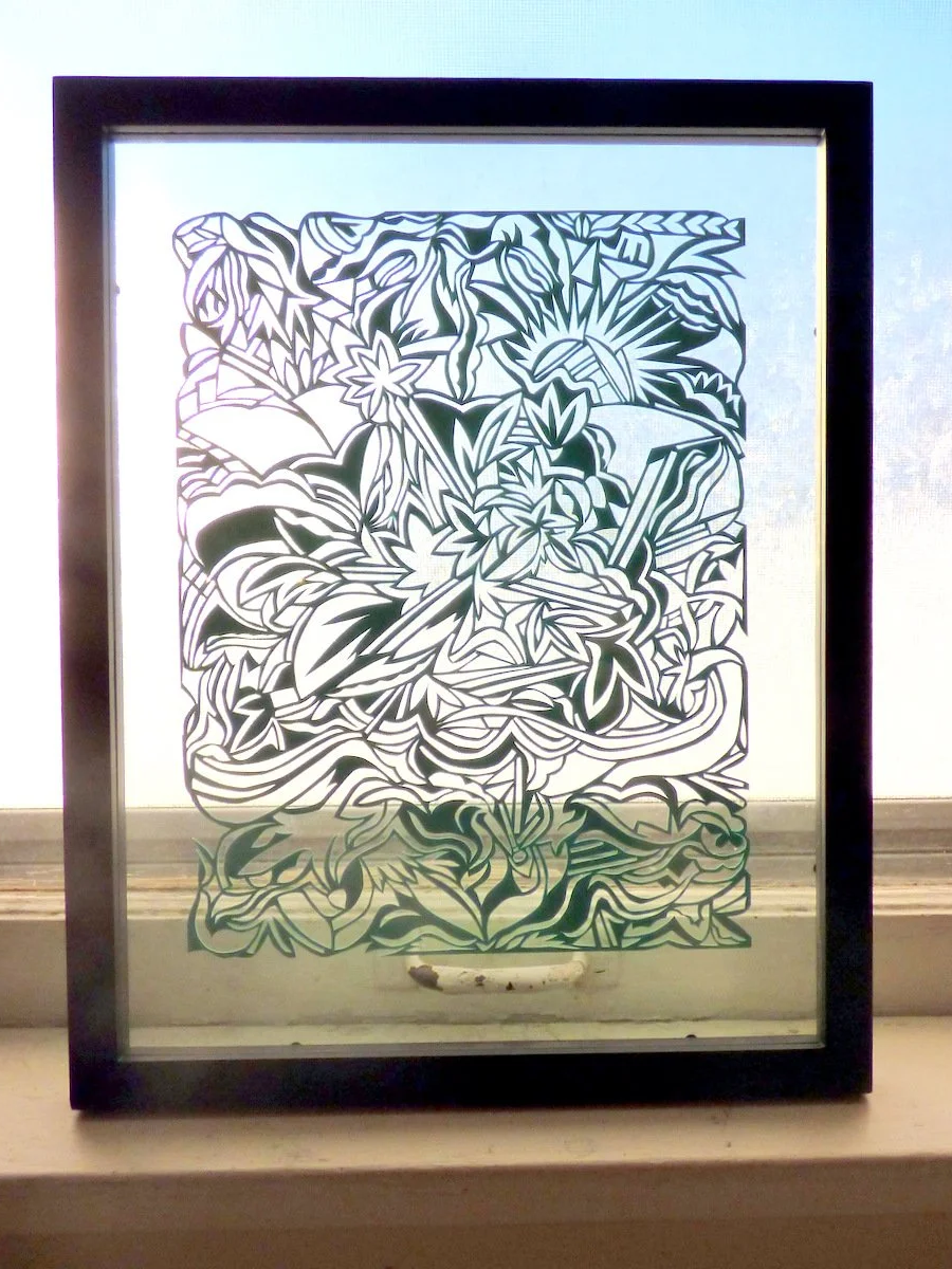 Decorative glass panel with abstract floral and leaf design, framed in black, reflecting light.