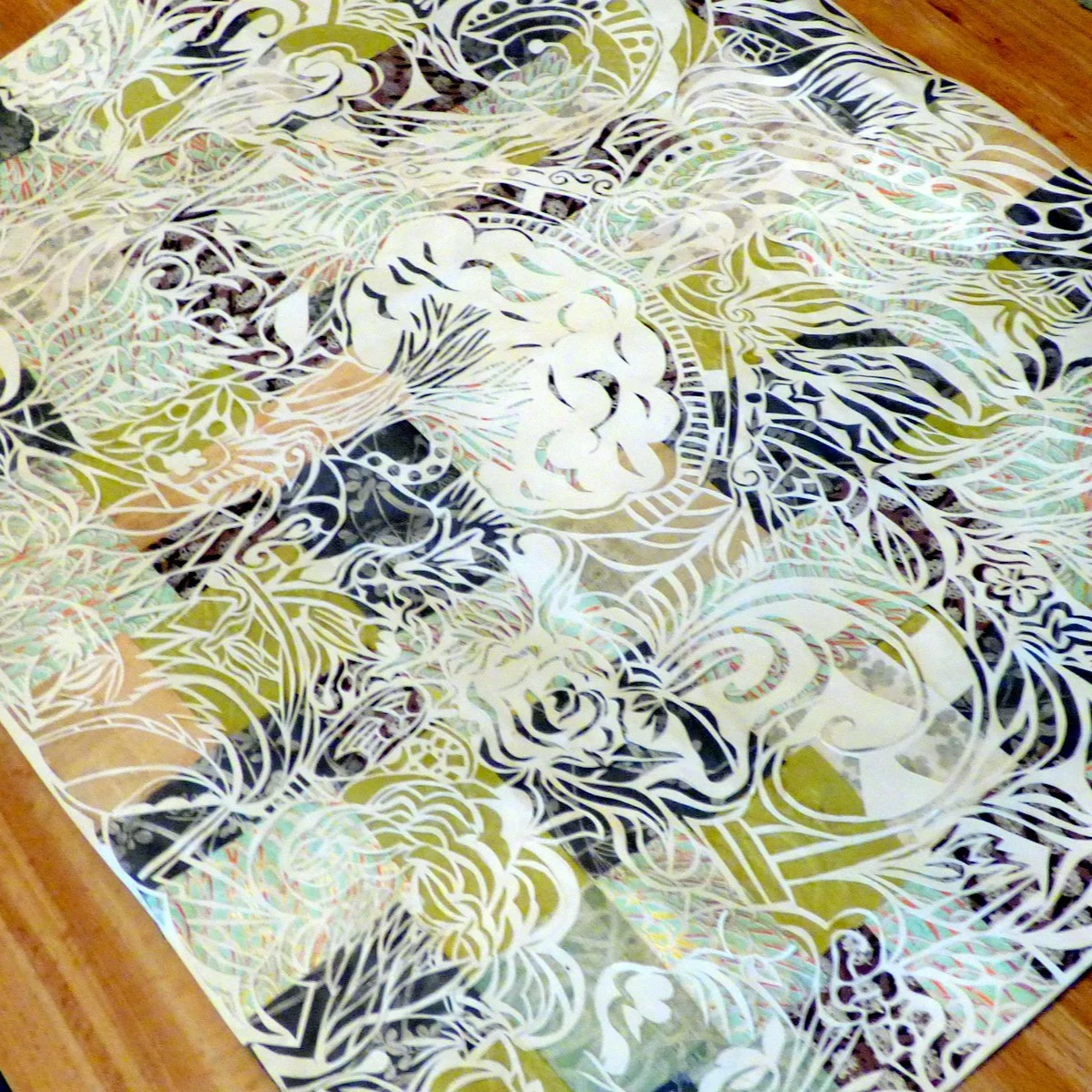 A colorful piece of art with intricate floral and abstract patterns in shades of yellow, black, white, and pastel colors on a hardwood floor.