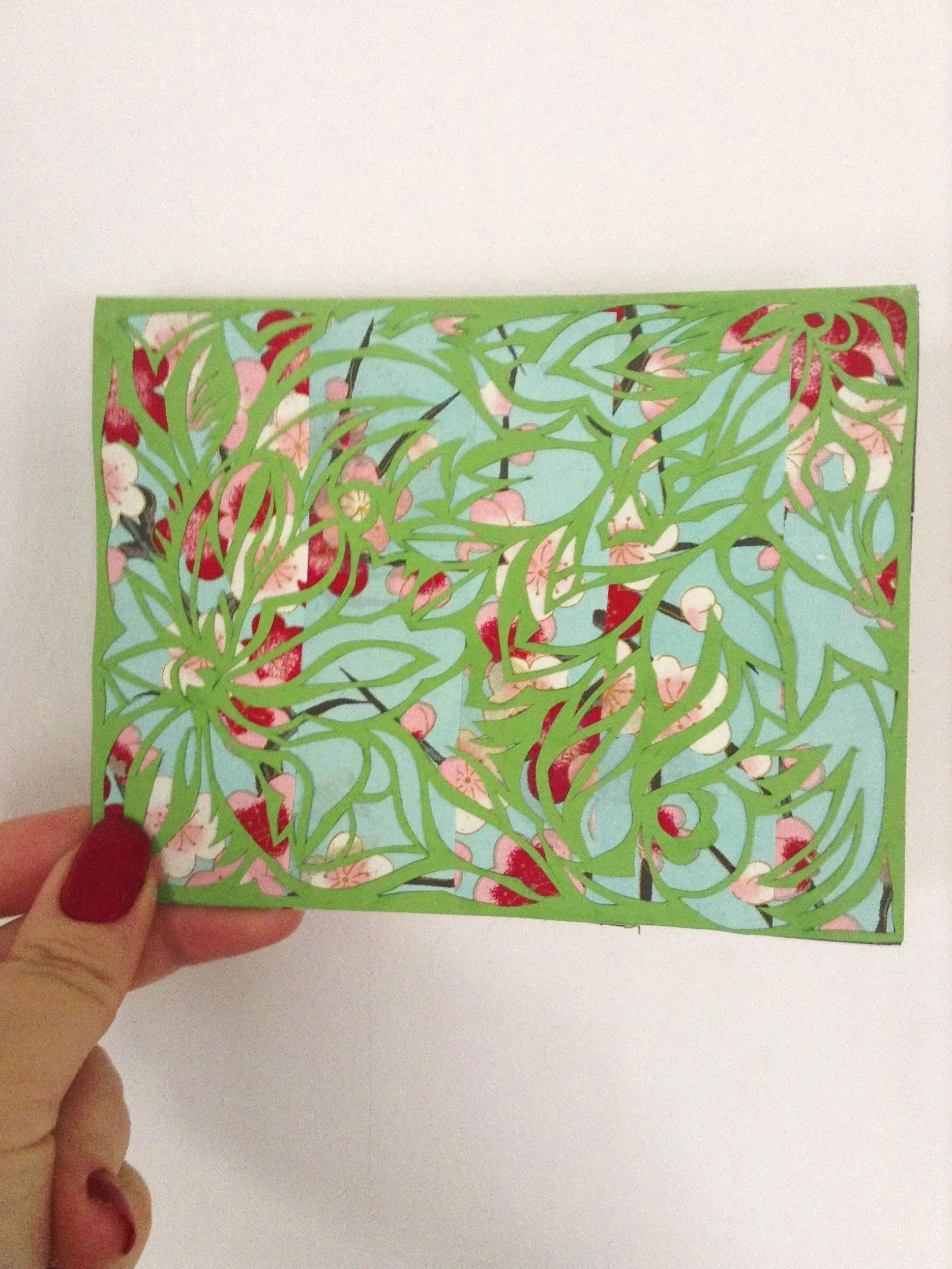 A person holding a colorful paper cutout with floral and leaf designs against a white background.