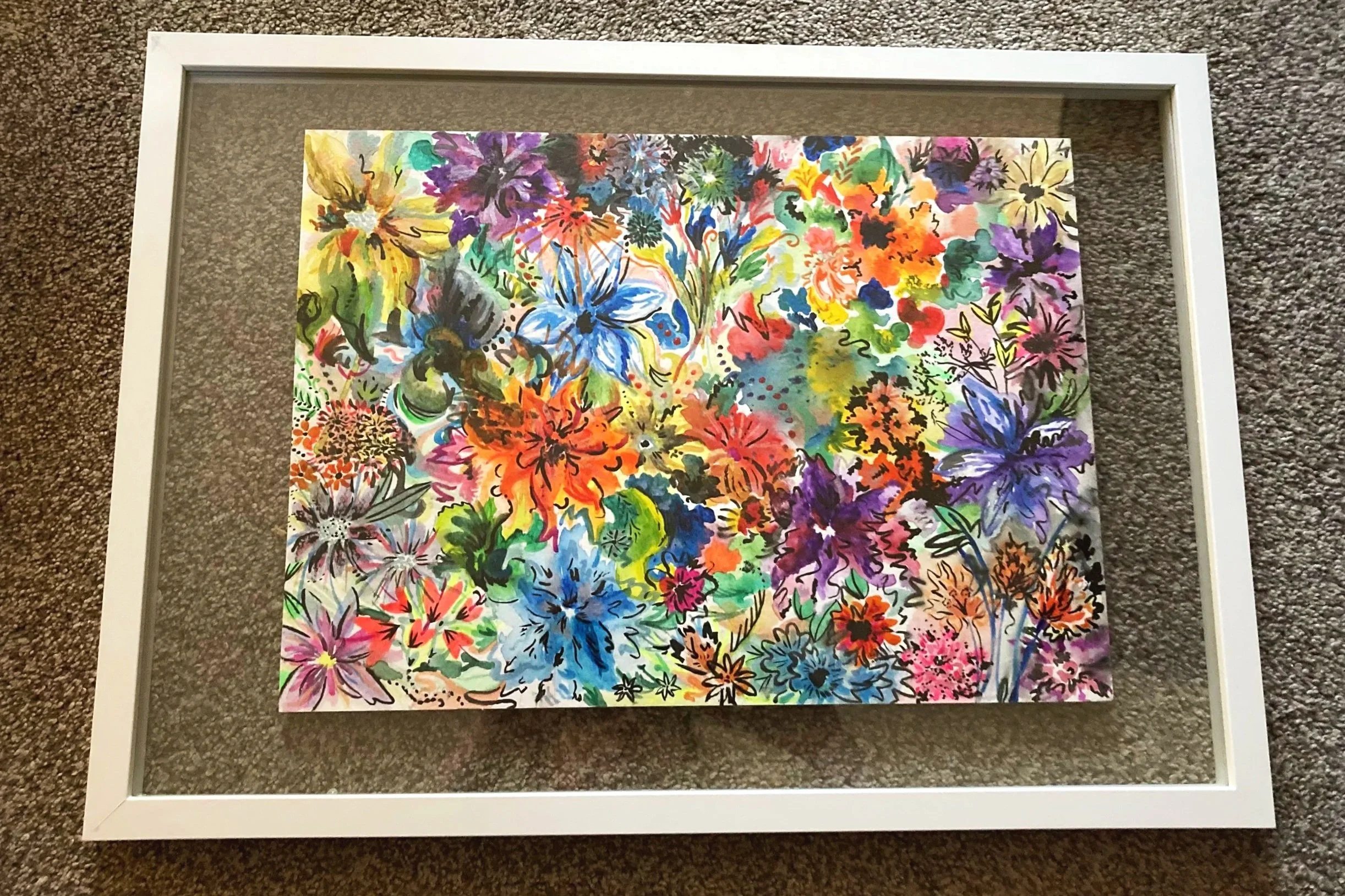 Colorful abstract floral watercolor painting framed in a white border, placed on brown carpeted floor.
