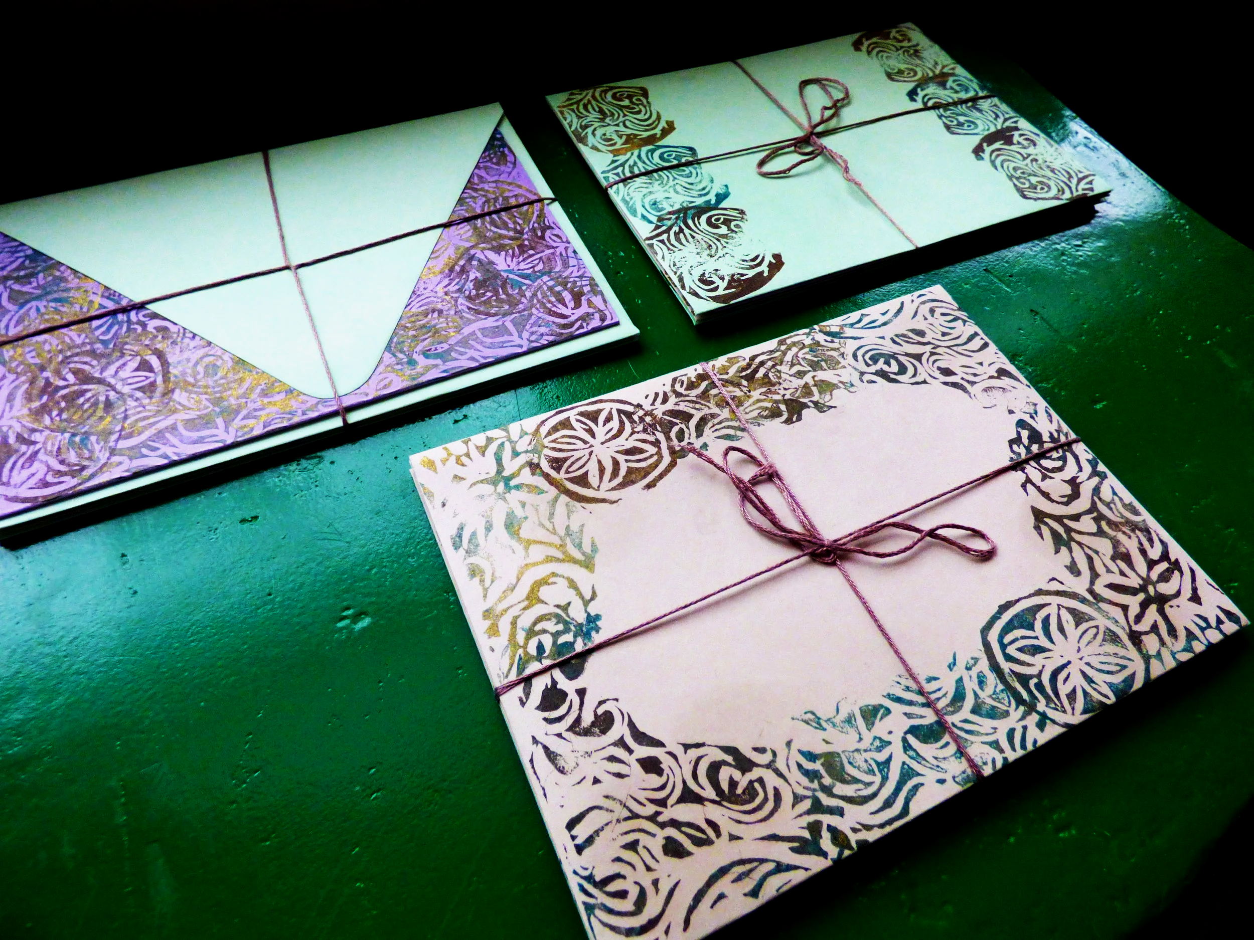Colorful elaborately patterned envelopes tied with pink string are displayed on a dark green surface.
