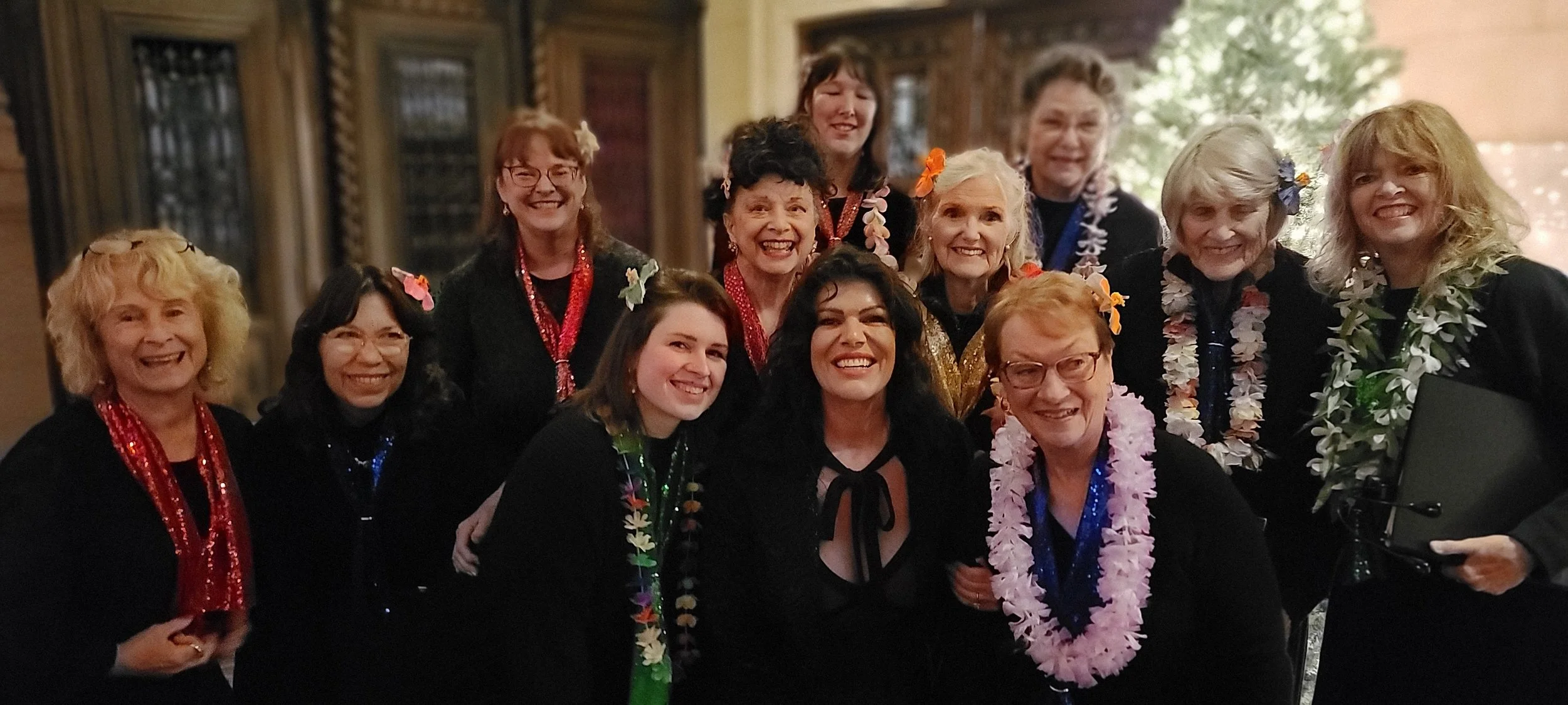 Group of women smiling and wearing colorful leis at an indoor celebration.