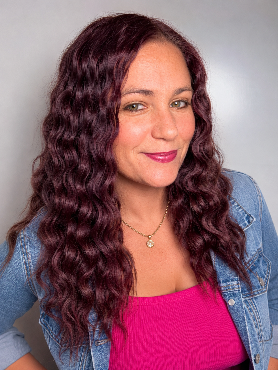 A woman named Jessica Shaker with long, wavy, dark red hair, wearing a pink top and a denim jacket, smiling slightly, against a light gray background.