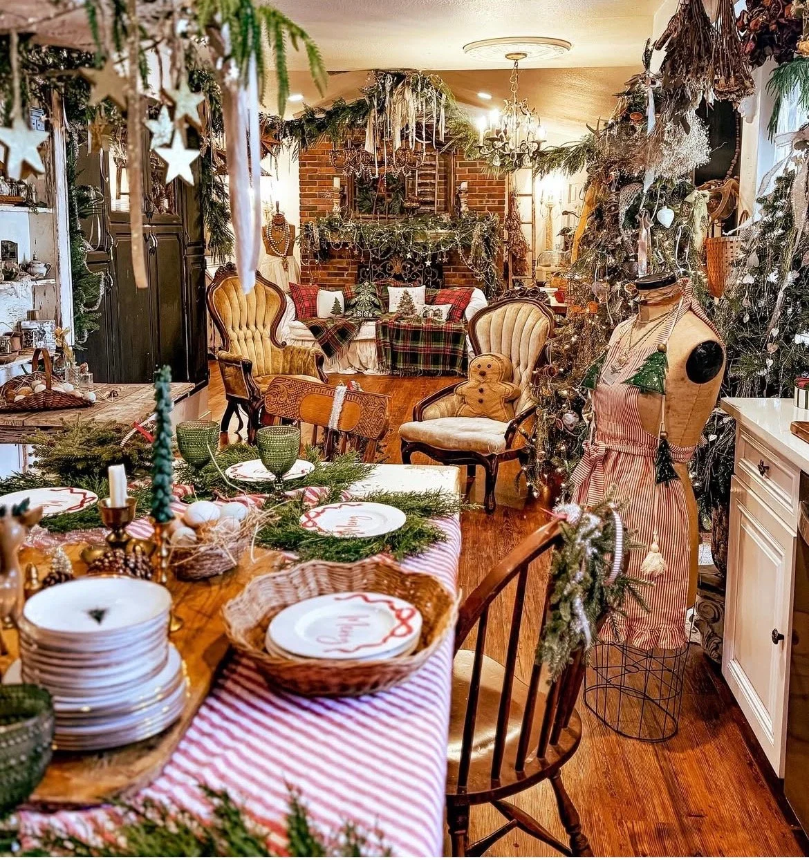 A festively decorated living room and dining area for Christmas with Christmas-themed tableware, ornaments, and holiday decorations including a gingerbread man on a chair, a decorated Christmas tree, and garlands.