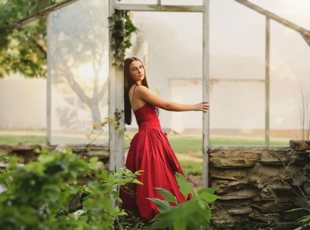 A young woman in a red dress standing in front of a greenhouse in a garden setting.