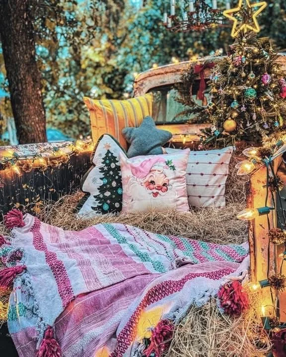 Decorated Christmas scene with a Christmas tree, pillows, blankets, and fairy lights outdoors