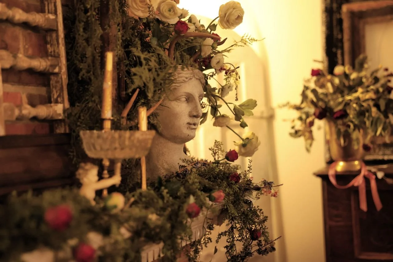 A decorative arrangement featuring a classical bust surrounded by flowers and greenery in warm, ambient lighting.
