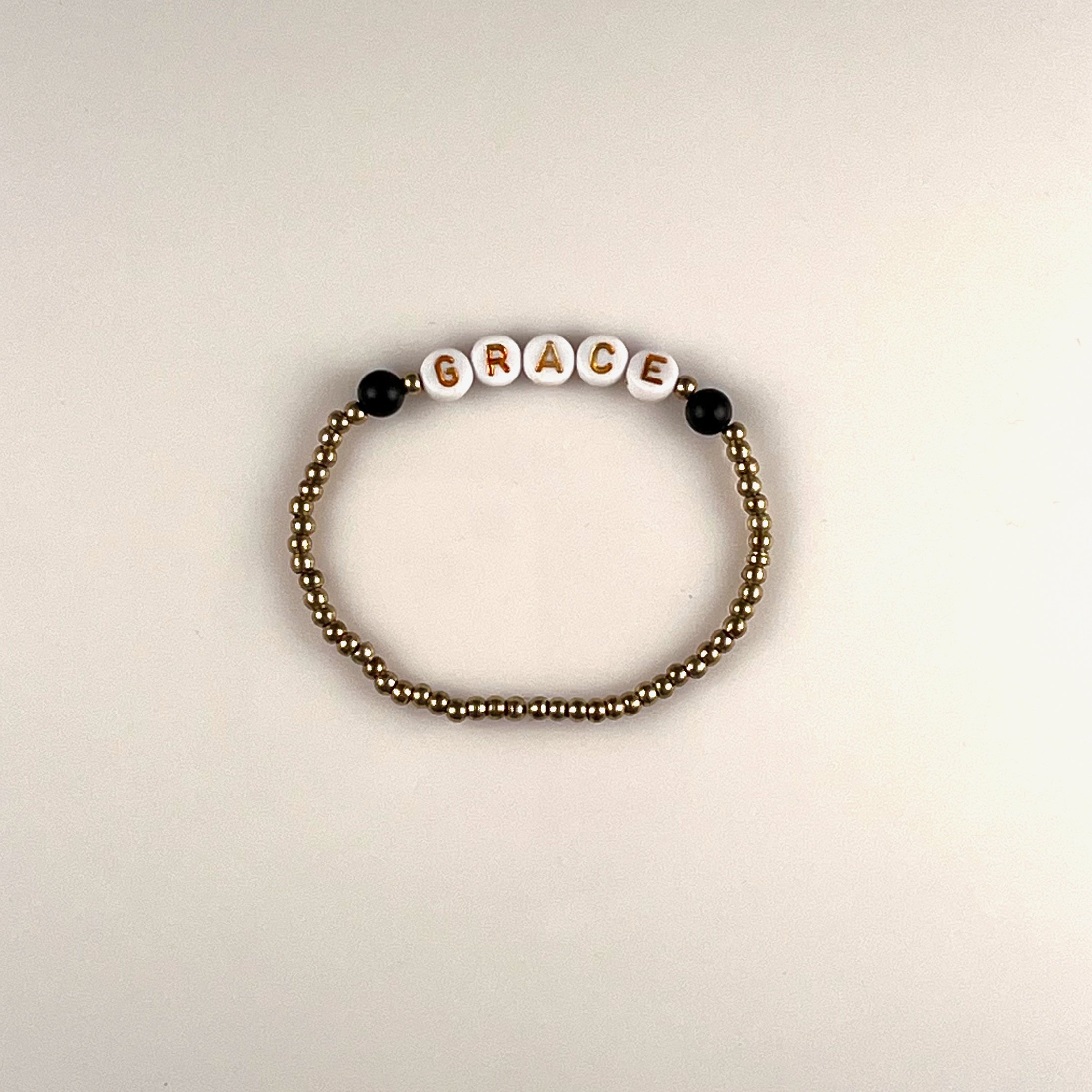 Grace: A customizable bracelet made with gold seed beads, black matte glass beads and gold letters on white beads. Personalize with a name or your favorite word. Up to 10 letters. $25 