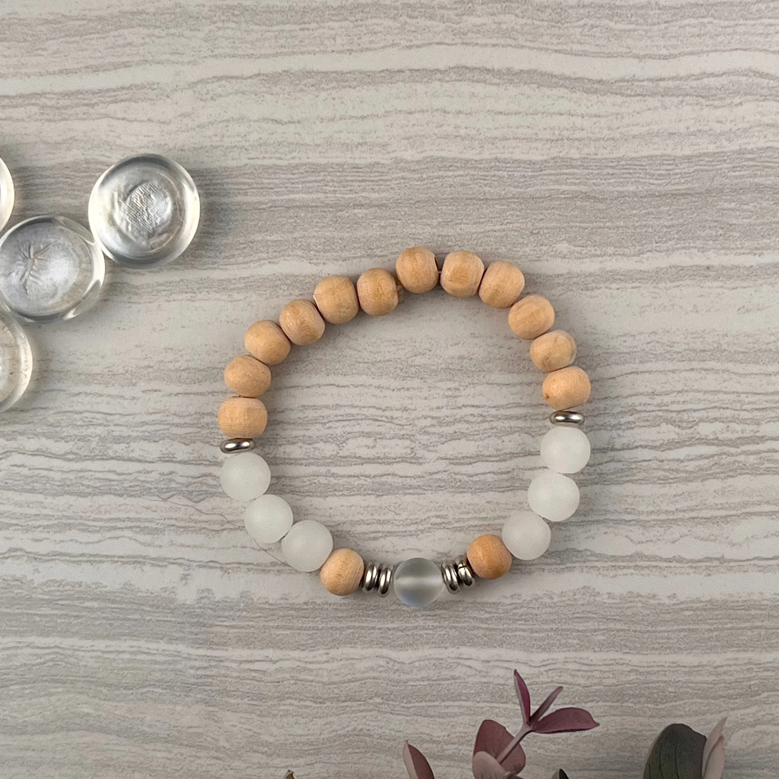 Shoreline Glow: Natural wood beads paired with frosted white glass and shimmering iridescent accents, completed with silver spacer beads. A soft, coastal inspired piece with a touch of sparkle. $20