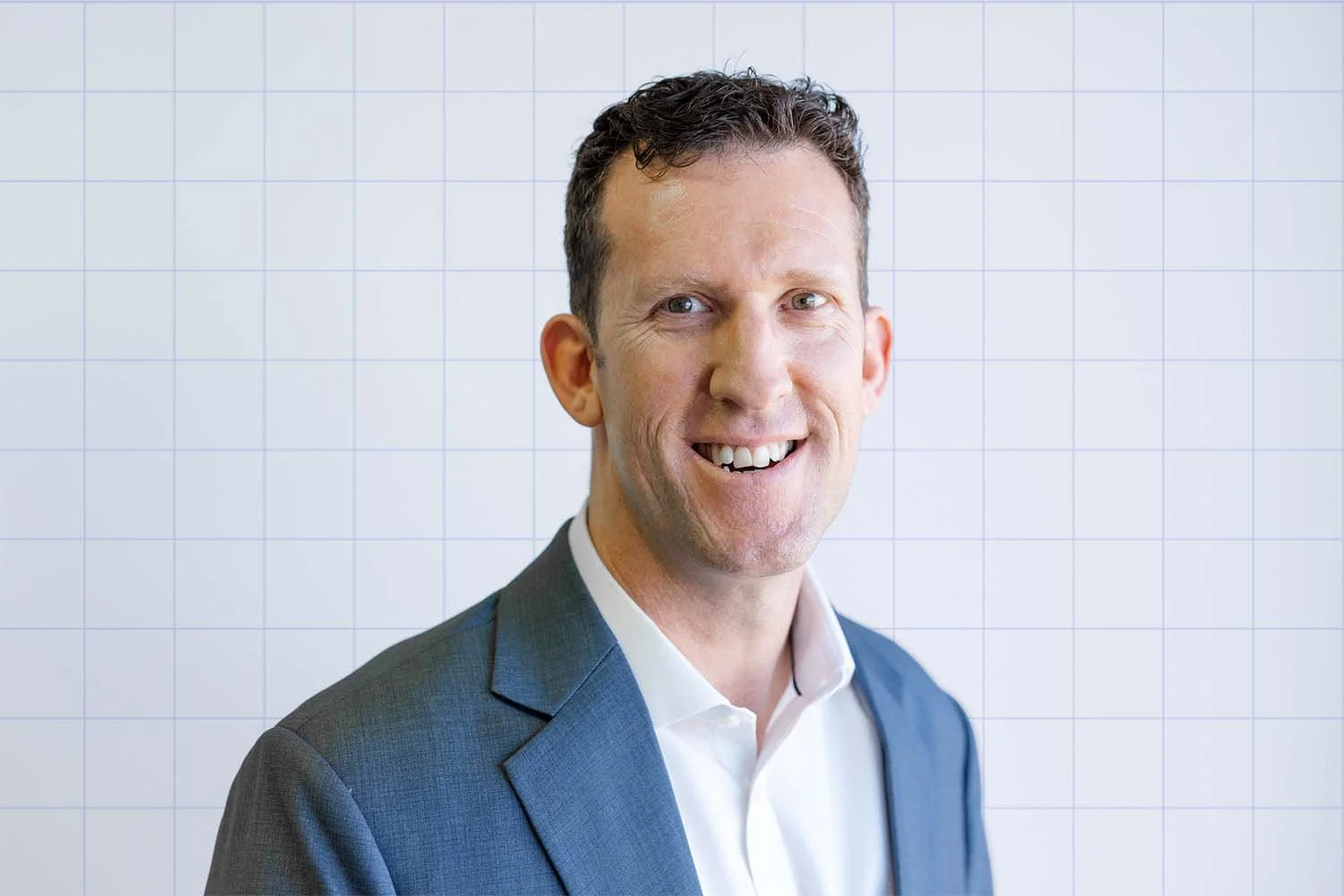Simon Johnson, financial adviser at TIPS Financial Services in Perth in a suit smiling in front of a white grid wall.