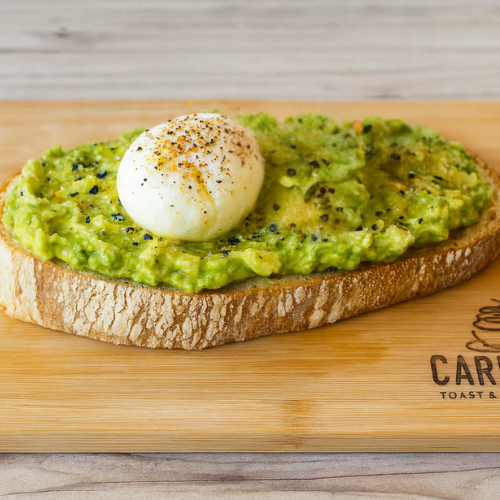 Toast topped with mashed avocado and a poached egg on a wooden cutting board.