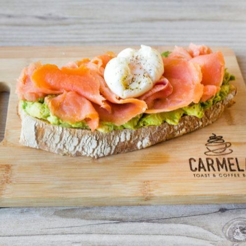 Open-faced smoked salmon and avocado toast with a poached egg on a wooden serving board.
