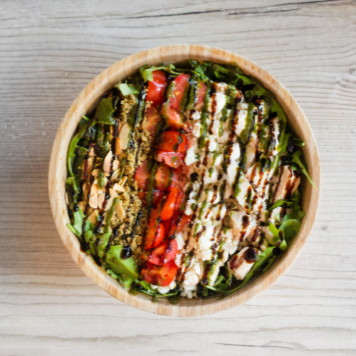 Bowl of sushi rolls topped with various sauces and garnishes, on a wooden surface.