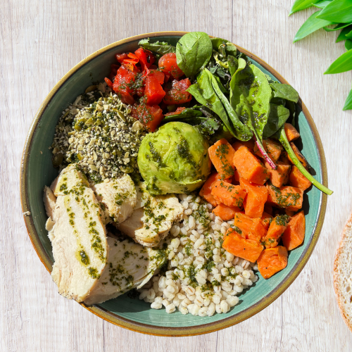 A bowl of mixed vegetables, grains, and chicken on a wooden table.