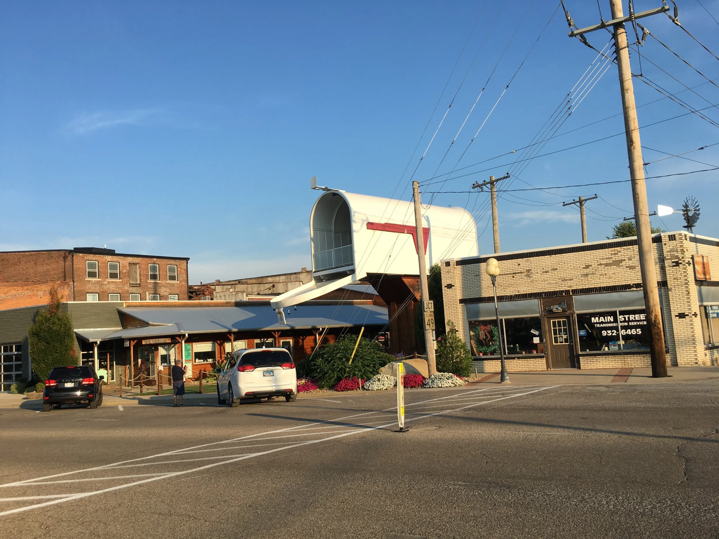 A giant mailbox in Casey, Illinois, stands above a main street. Cars are parked underneath as people walk on the sidewalk.