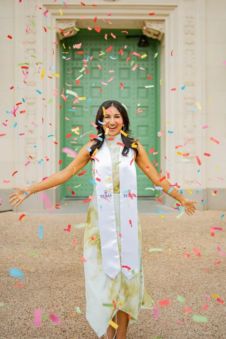 Woman celebrating graduation with confetti outside a building with a green door.