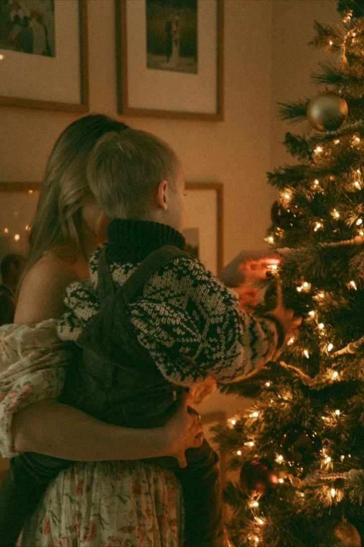A woman holding a child while decorating a Christmas tree at night.